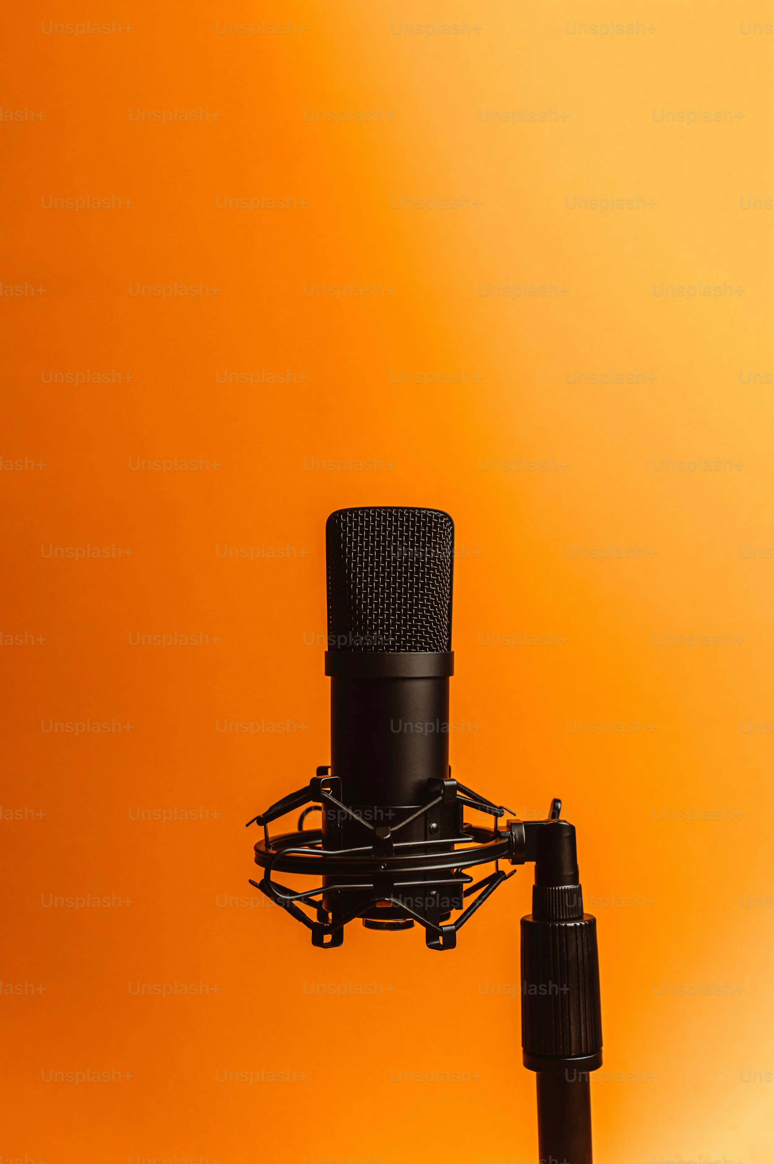 Close-up of a professional microphone on a stand against an orange background.
