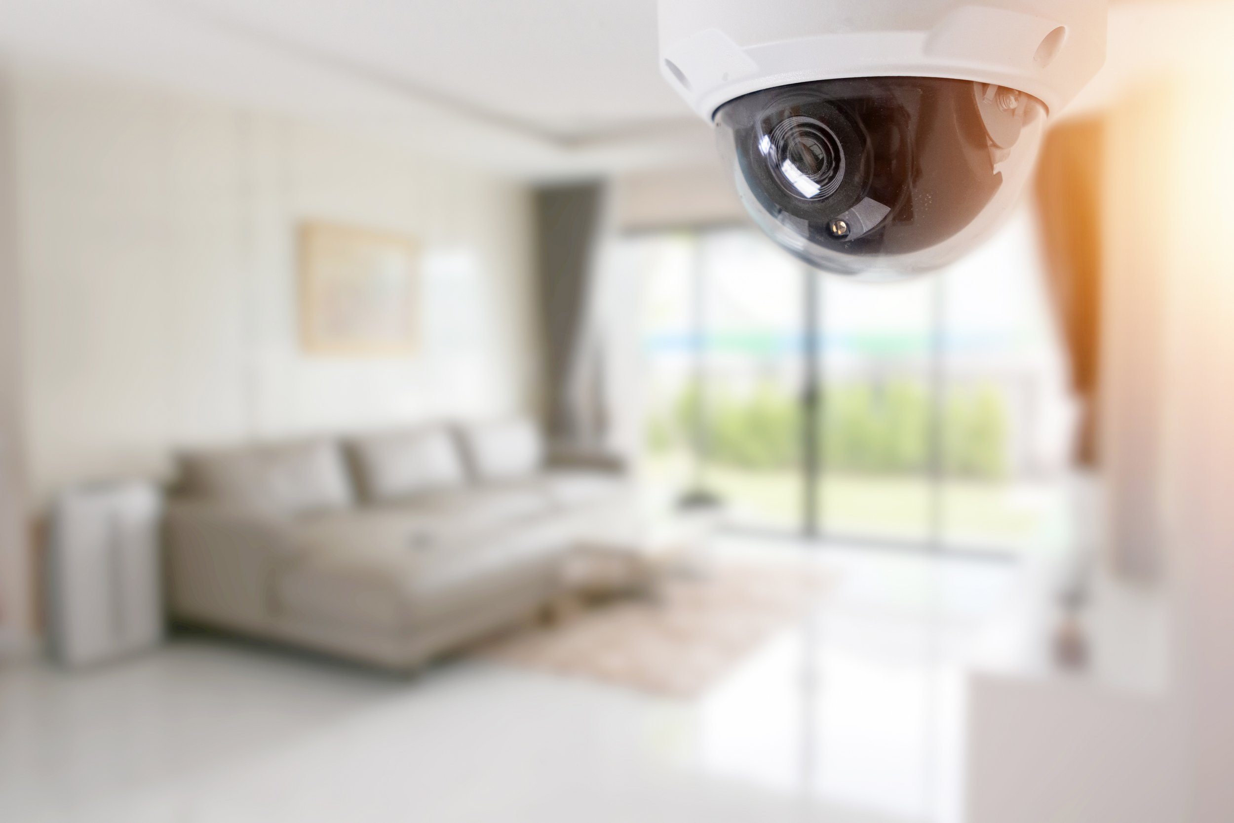 Security camera inside a room with a sofa, large window, and bright natural light.