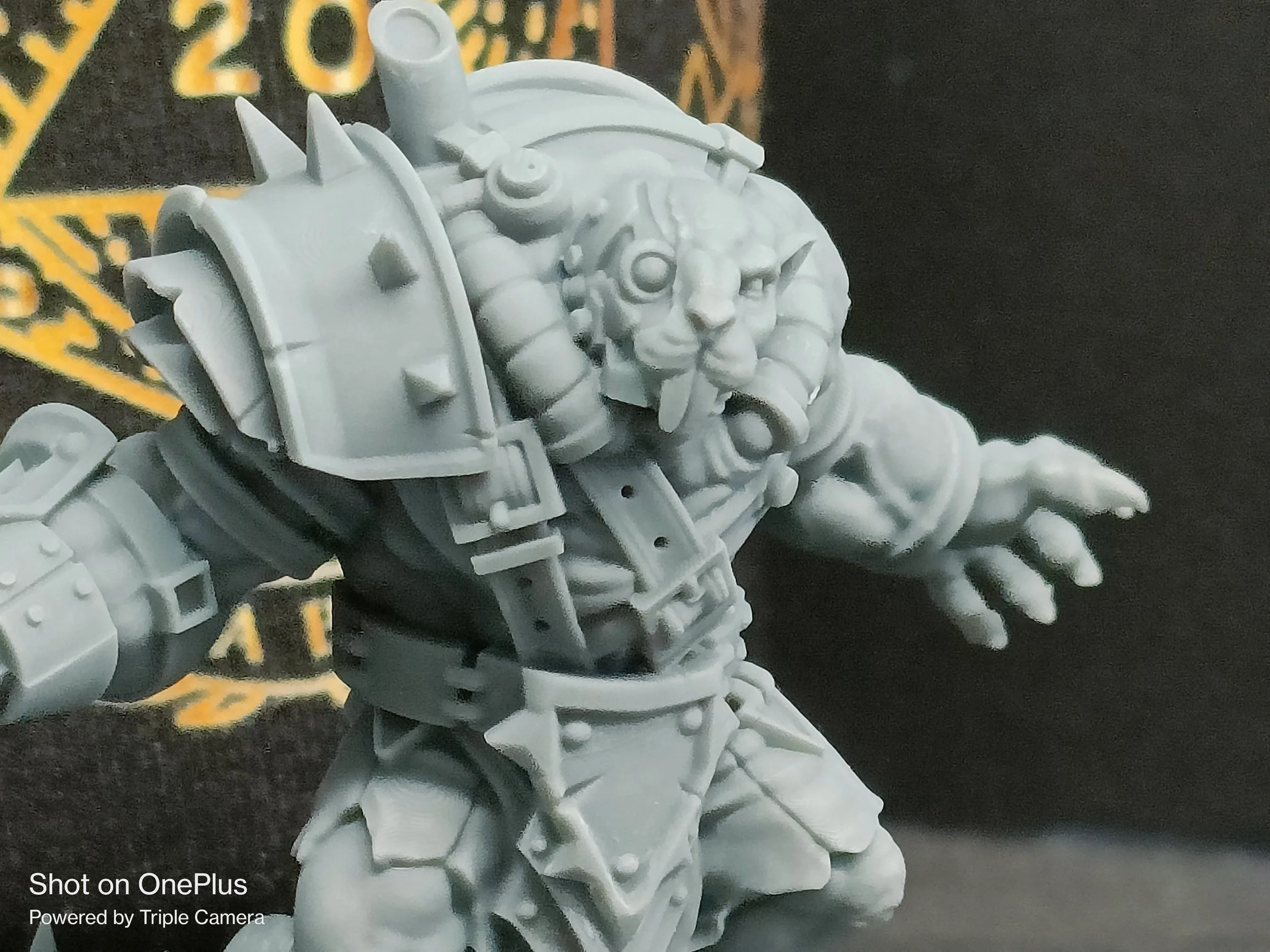 Unpainted miniature figurine of a fantasy creature resembling a beastman with a lion-like face and horns, wearing armor and a backpack, on a dark surface with some text in the background.