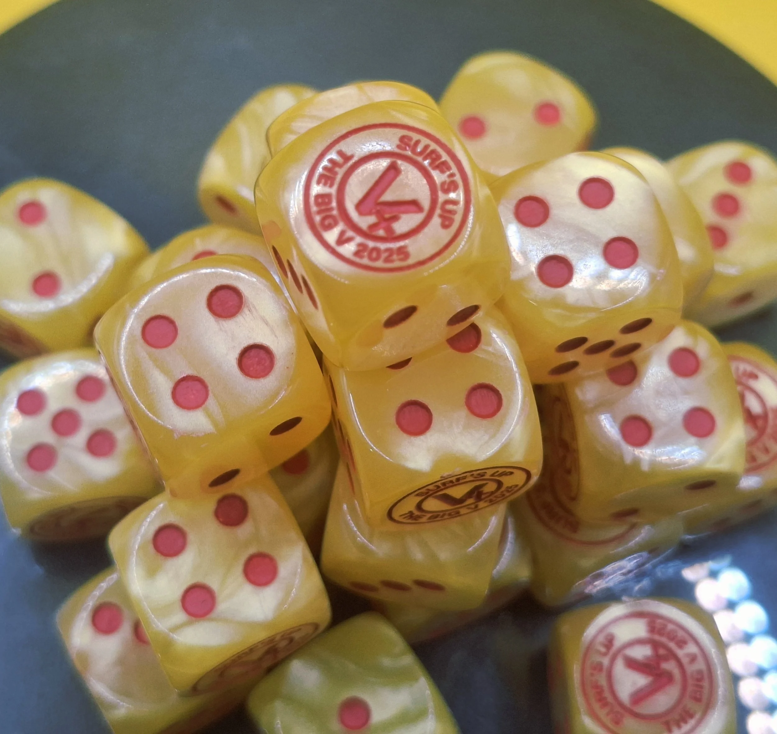 Close-up of yellow dice with pink dots, featuring a logo with the number 4 and the words 'Super Dice' and 'Official Ball' printed on some of the dice.