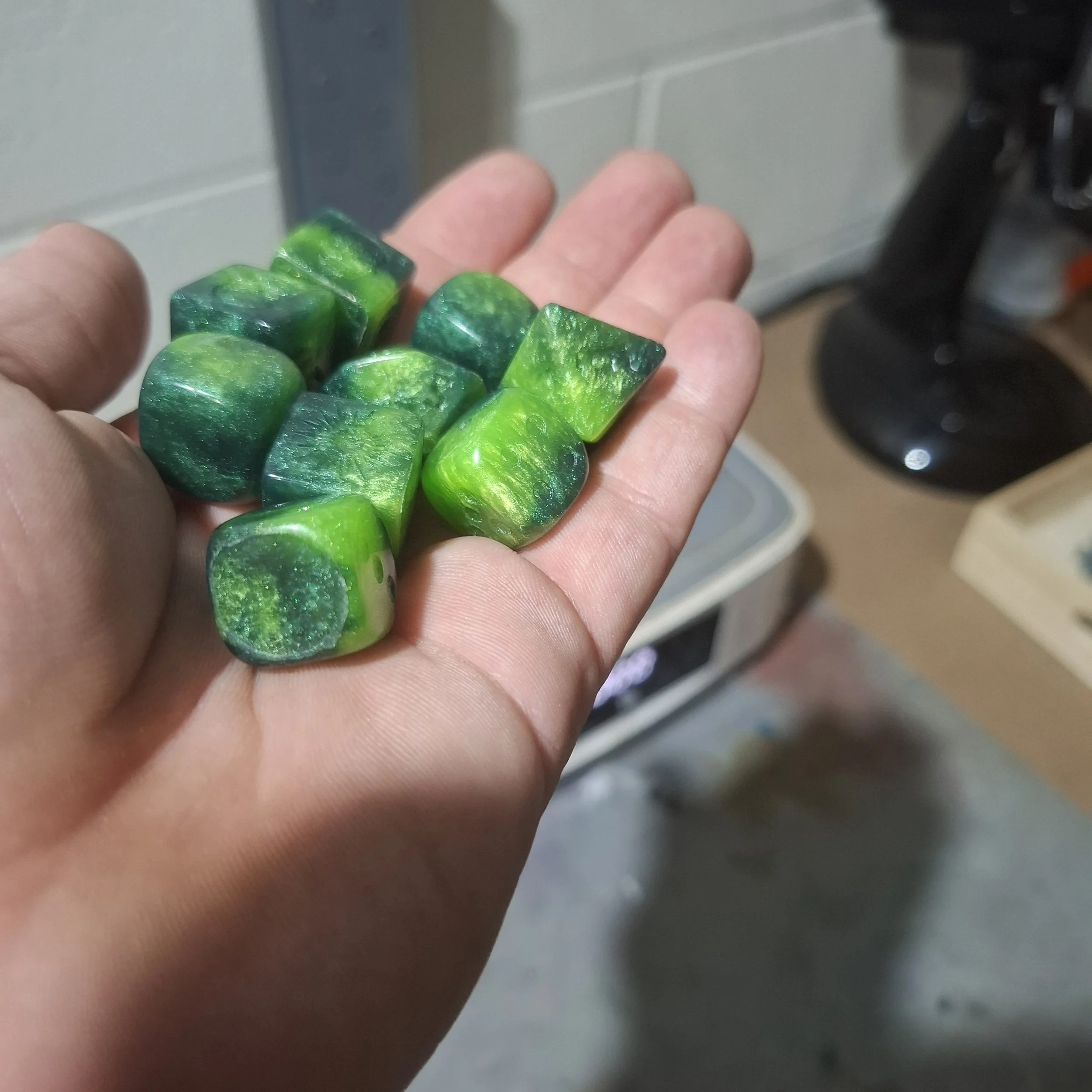 Hand holding small green and yellow marbled stones or gemstones.