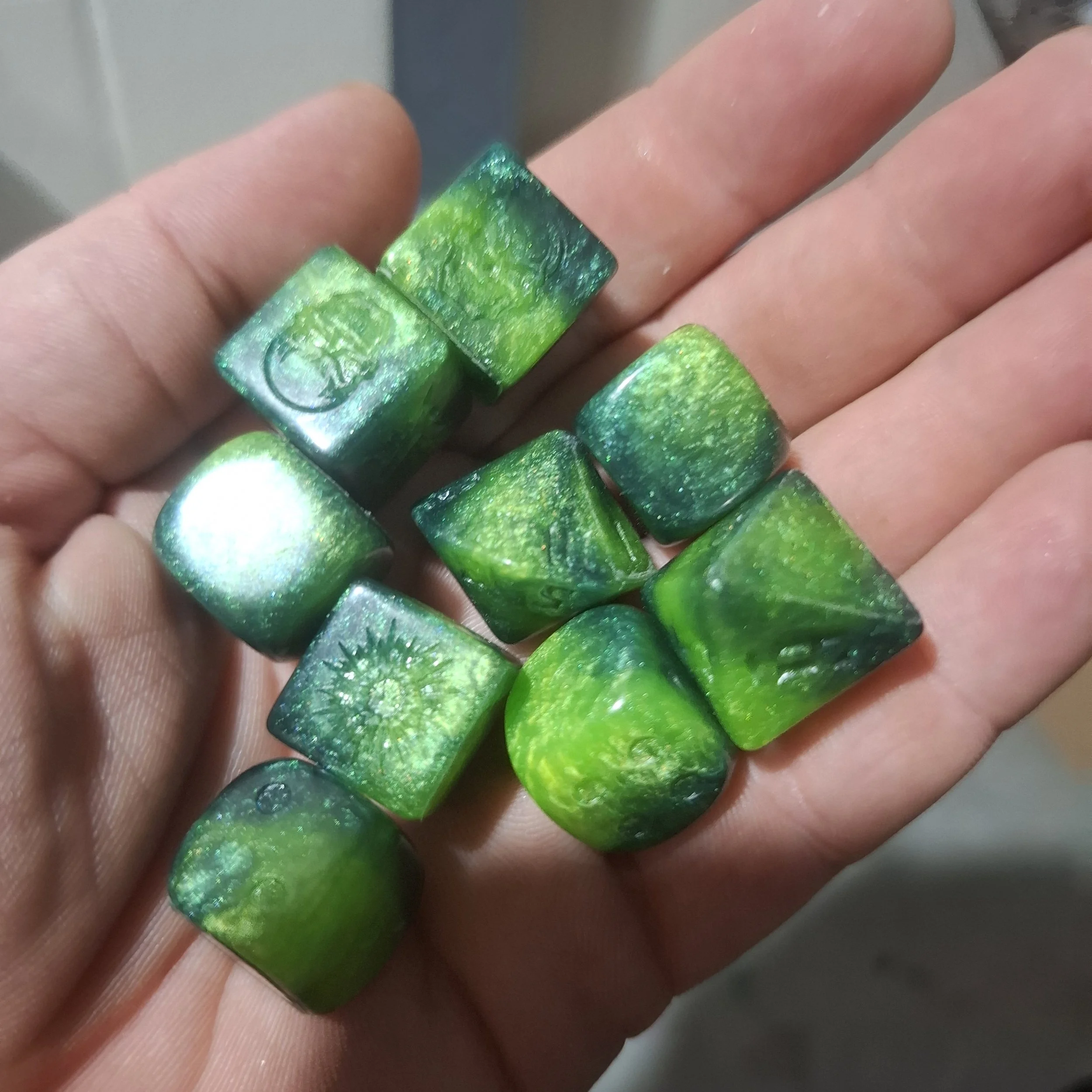 A person's hand holding shiny, green, square-shaped dice with a glittery appearance.