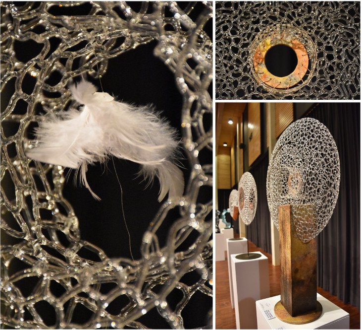 Œuvre d'art contemporaine composée d'une structure de verre complexe, une plume blanche, et des sculptures modernes en forme de sphères avec des motifs délicats.