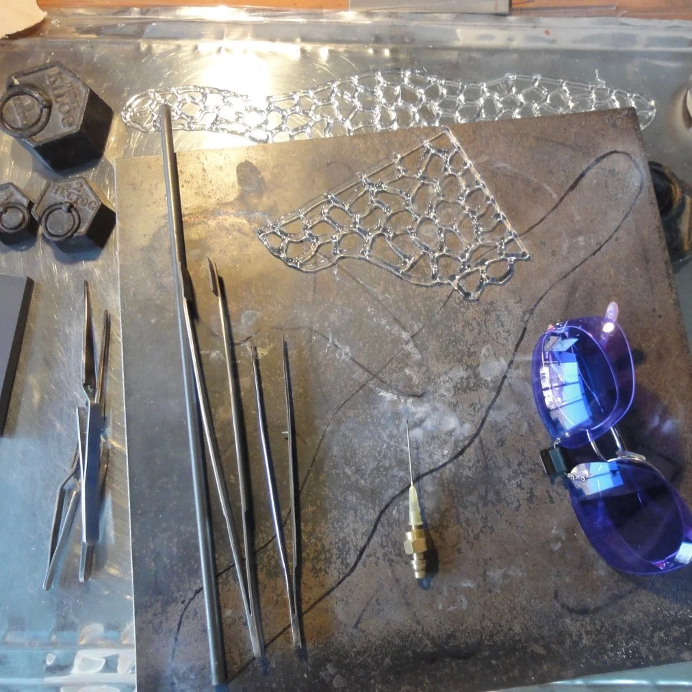 Petits outils de travail du verre à chaud au chalumeau avec lunettes de protection, sur une surface en métal.