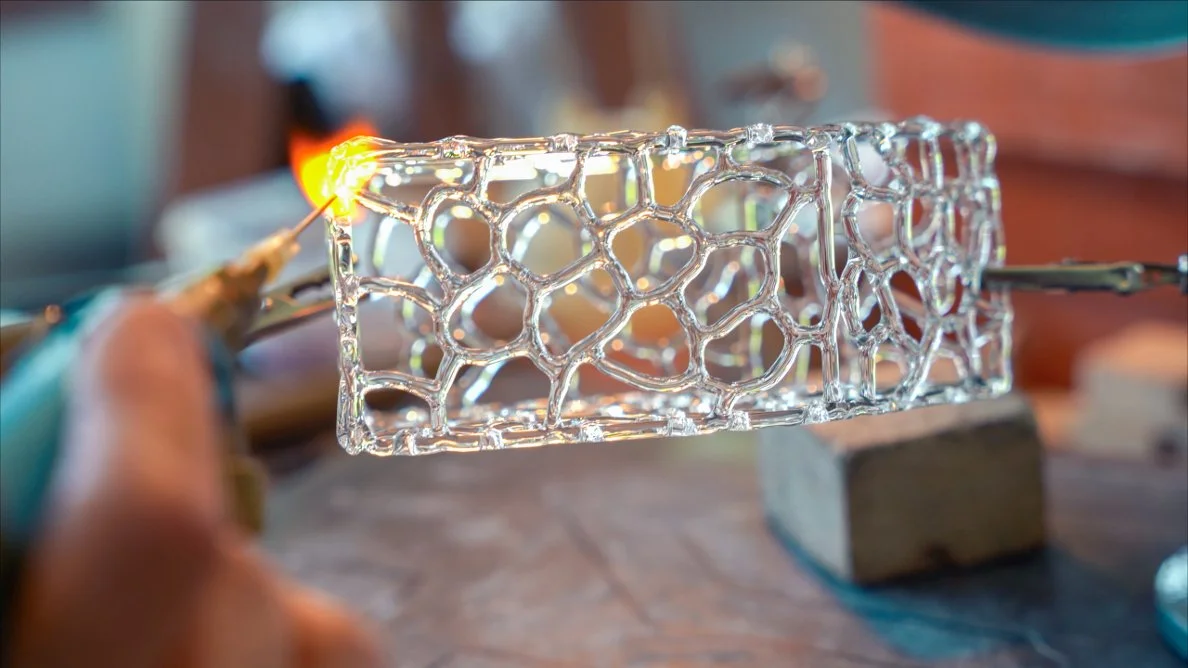 Il s'agit d'une pièce en verre avec un motif de dentelle. La pièce est en cours de fabrication avec un  chalumeau appliquée à un coin par l'artiste Corinne Joachim.