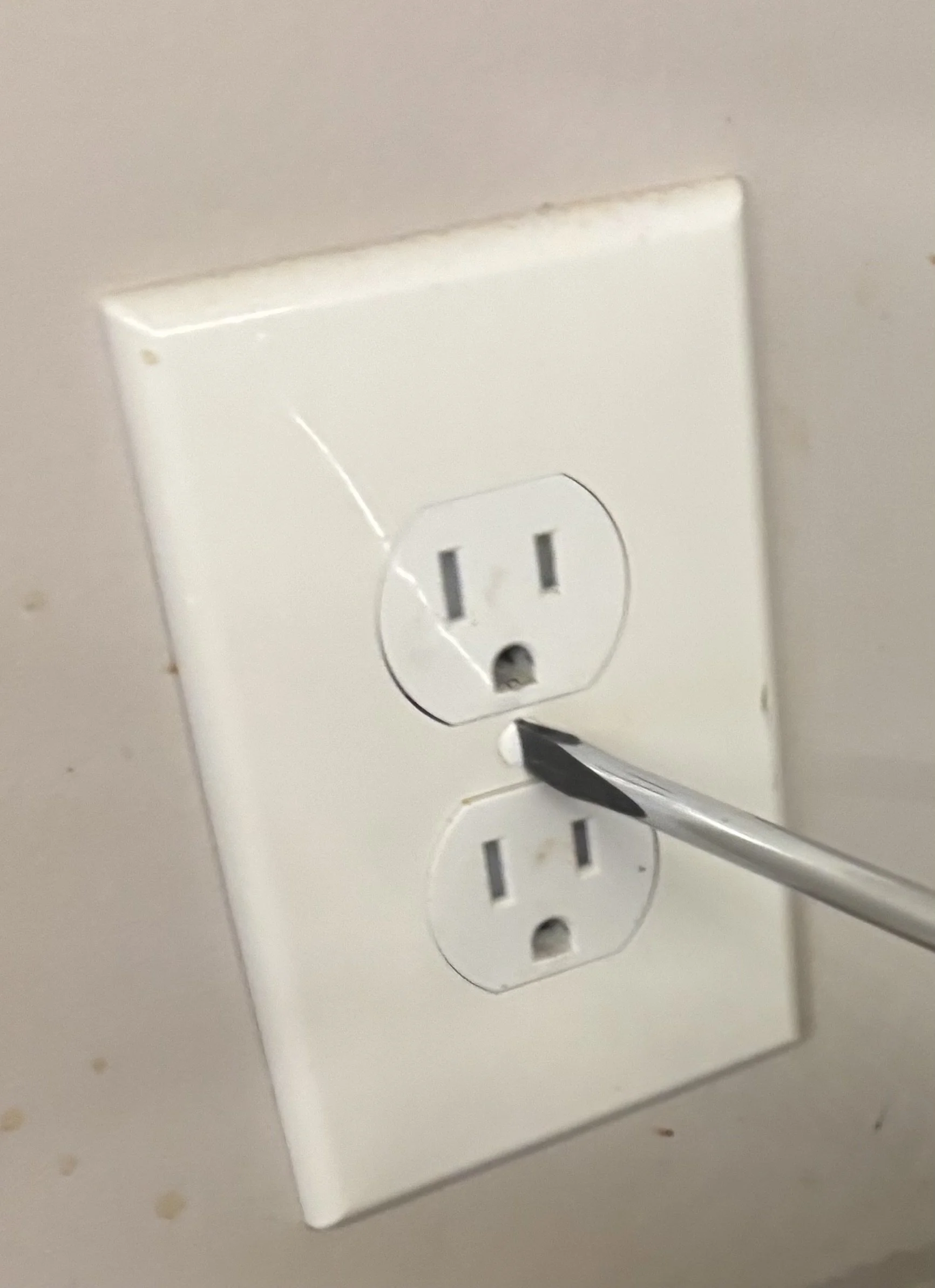 Close-up of a white electrical outlet with a screwdriver pressing into the lower socket