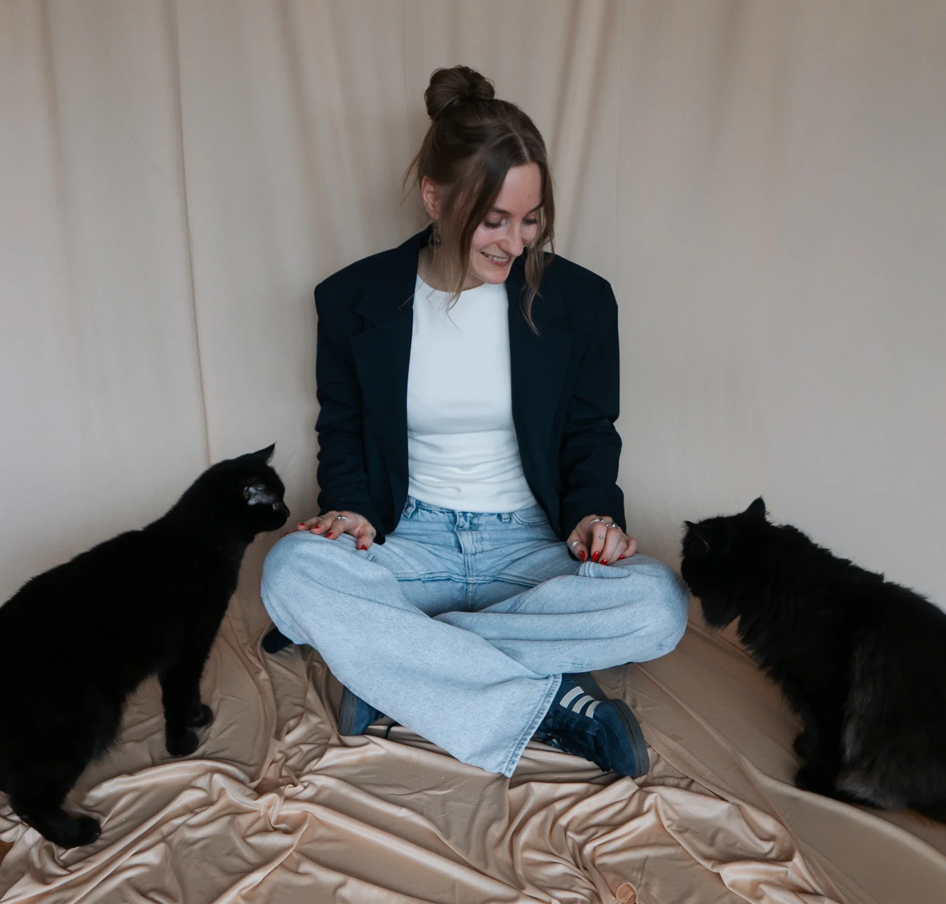 Lea sitzt mit ihren zwei Katzen vor einem beigen Hintergrund.