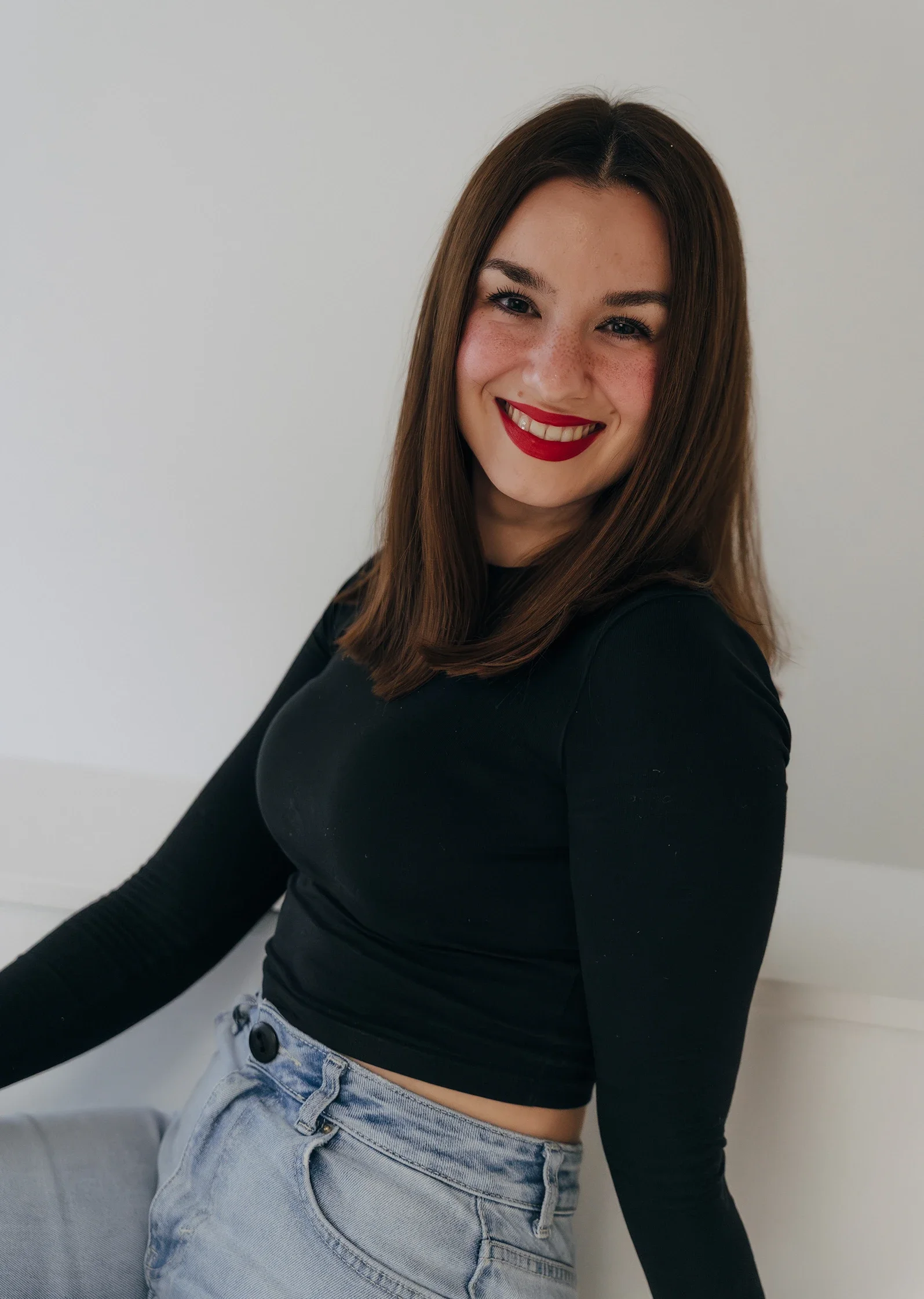 Laura, eine Kundin sitzt vor einer hellen Wand und lächelt in die Kamera.
