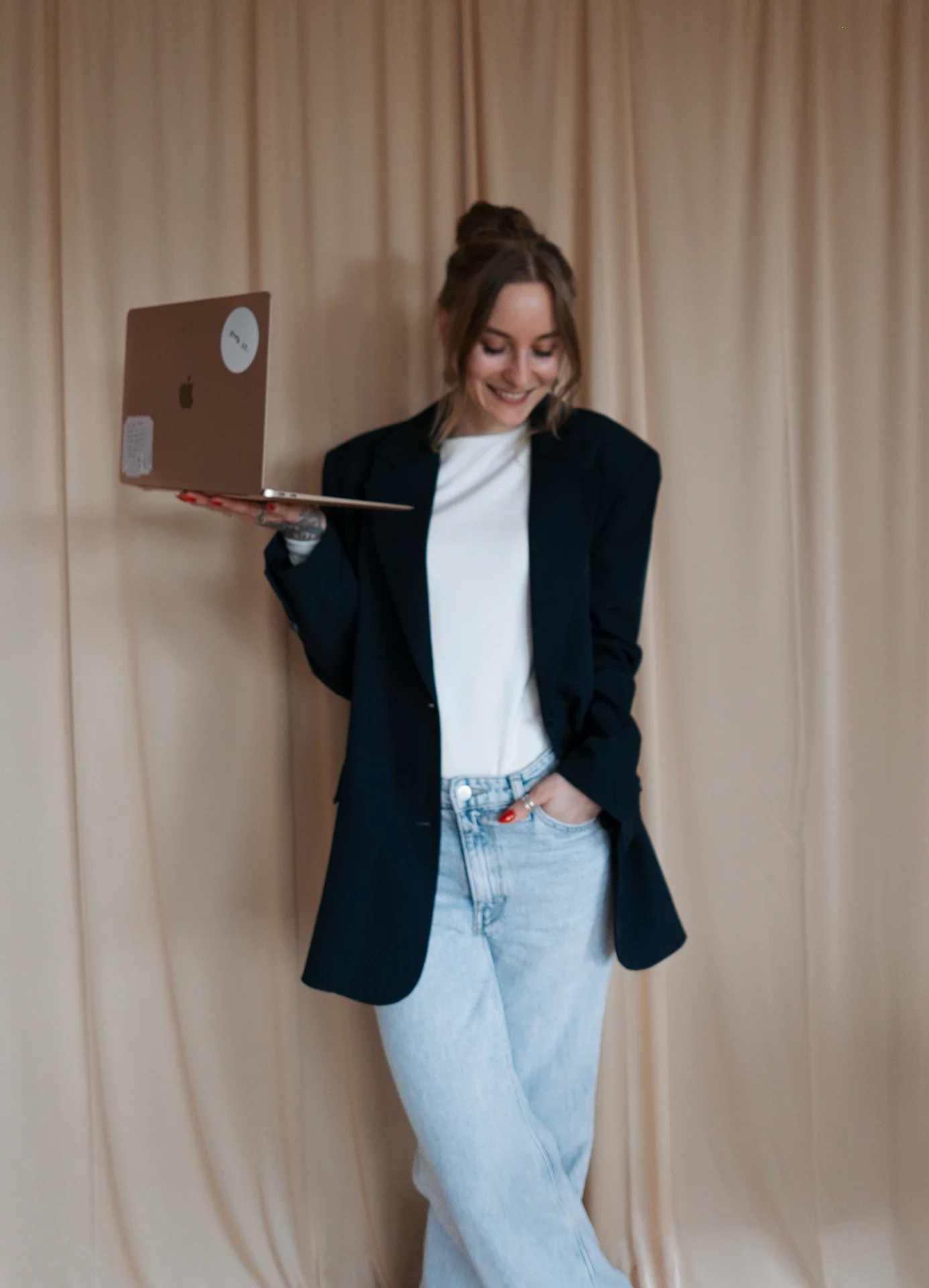 Lea steht mit ihrem Laptop vor einer beigen Wand.