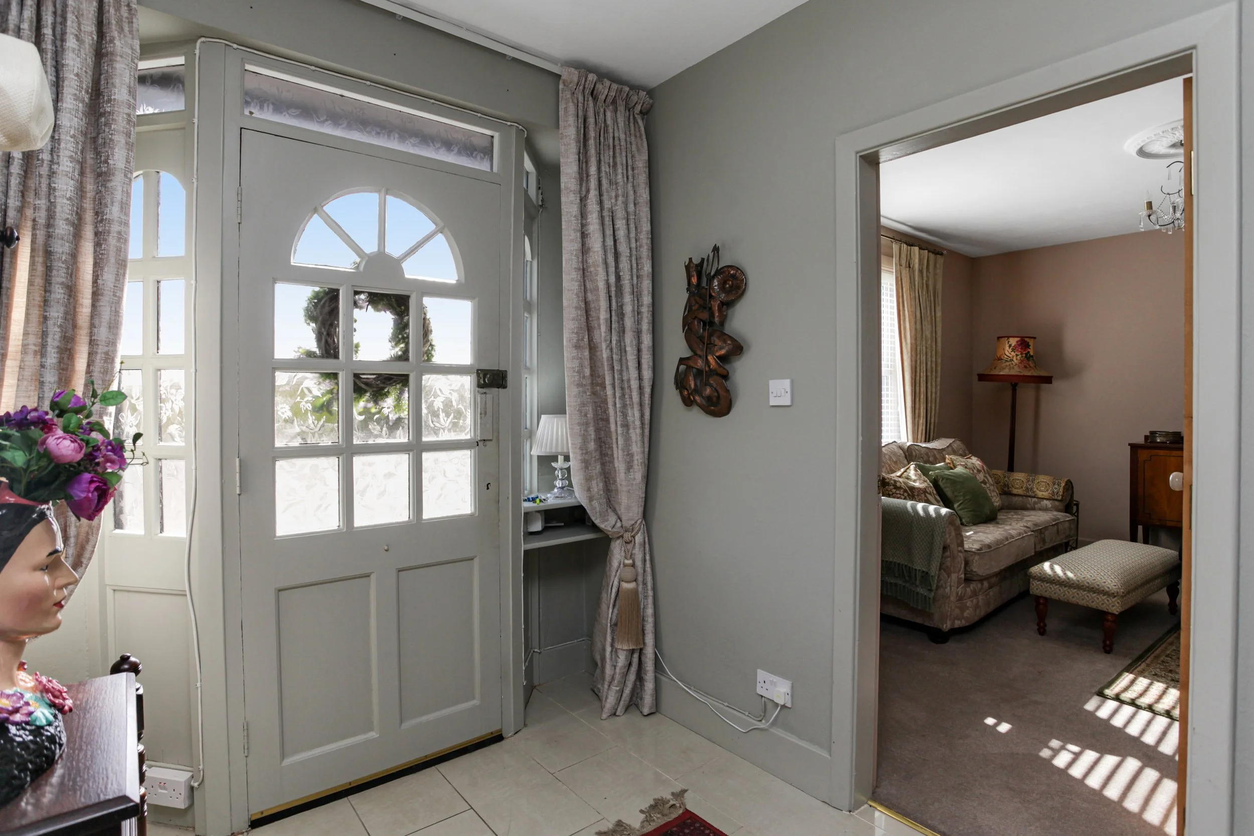 Entryway with front door and a view into a living room with a sofa and a standing lamp.