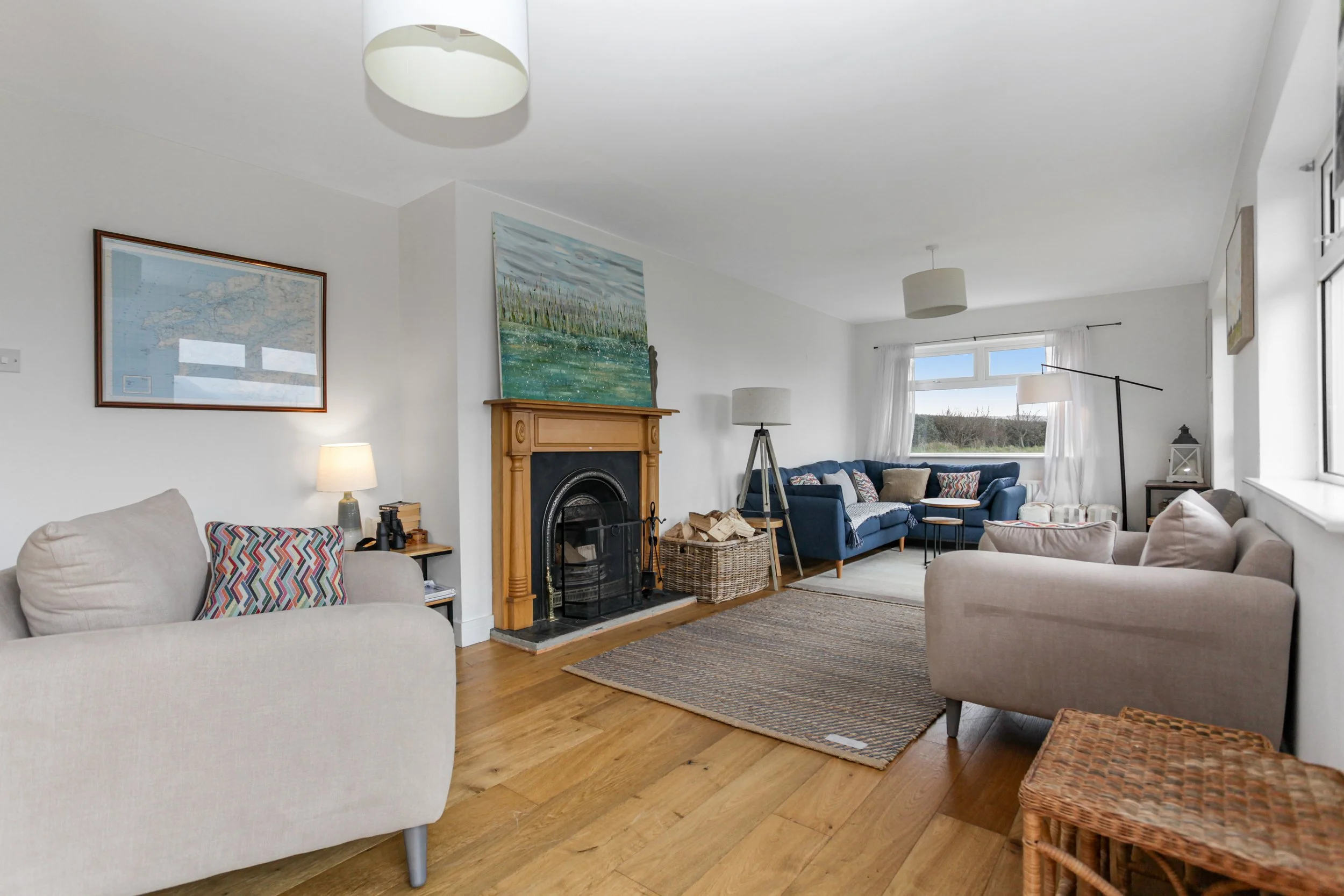 Living room with beige, blue, and gray sofas, a wooden fireplace, a patterned rug, and large windows allowing natural light.