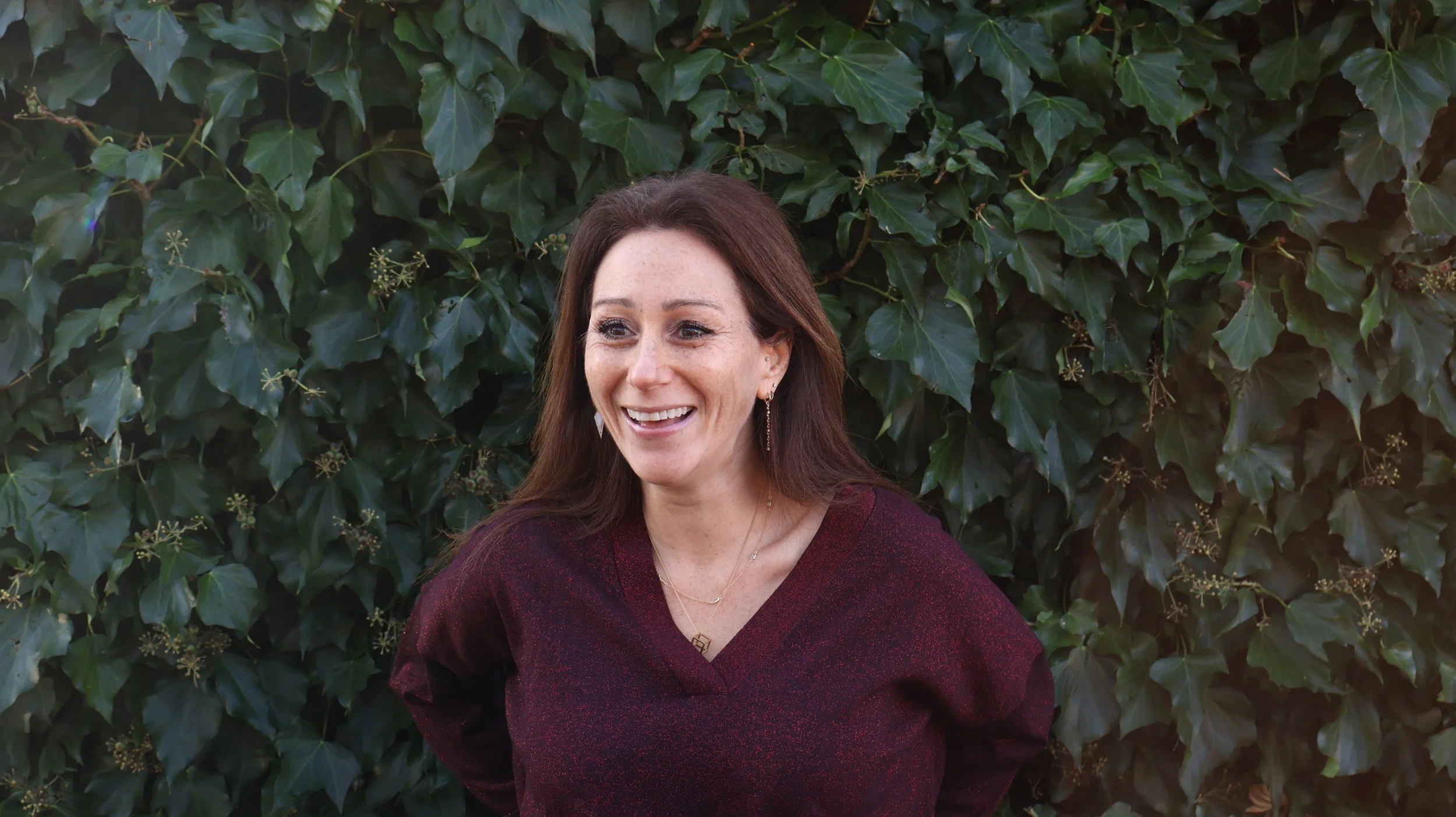 Psychologist standing in front of hedge smiling