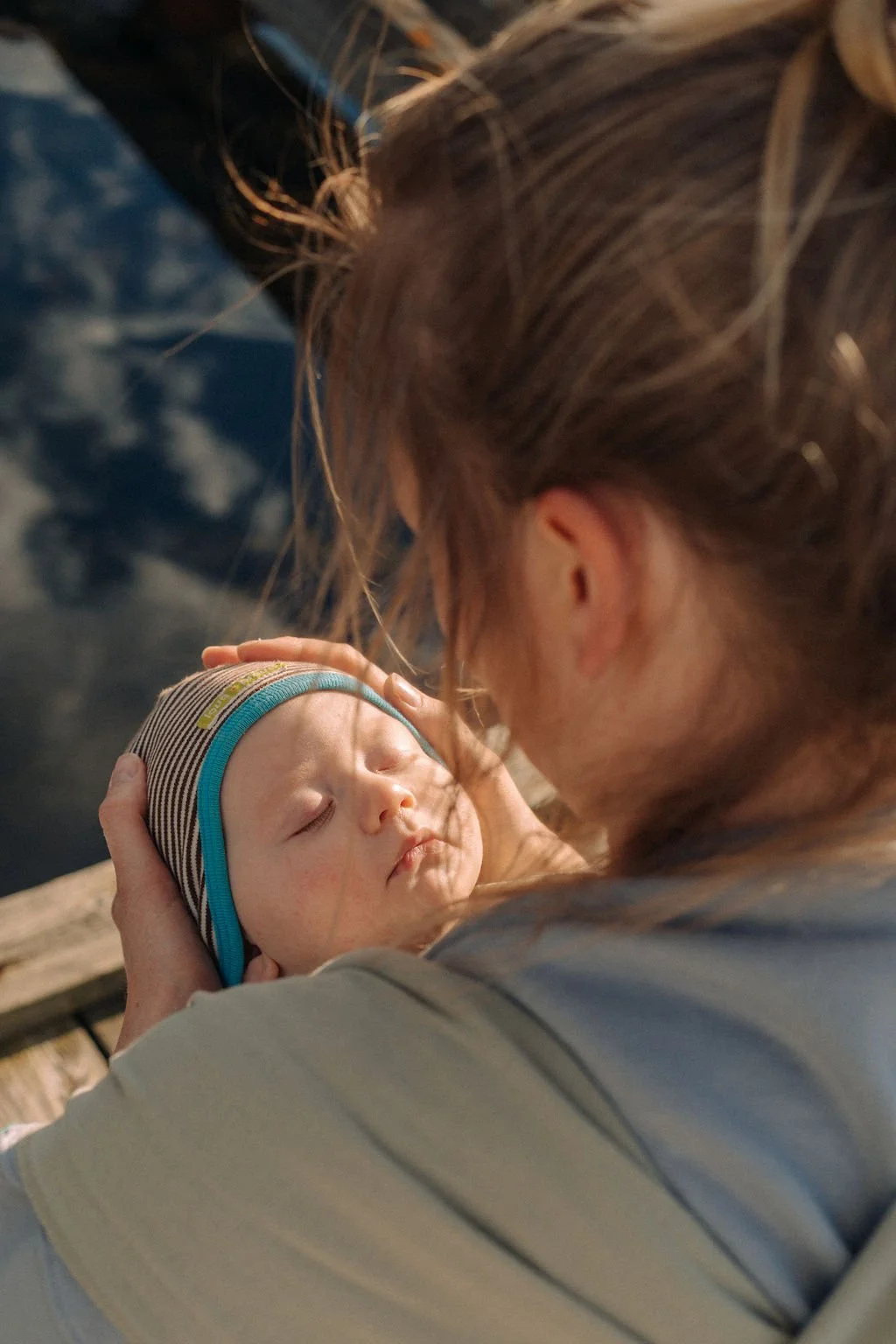 Ein Baby schläft sanft im Arm einer Frau, die es hält, in einer warmen Szene, vermutlich im Freien oder in einem natürlichen Umfeld.