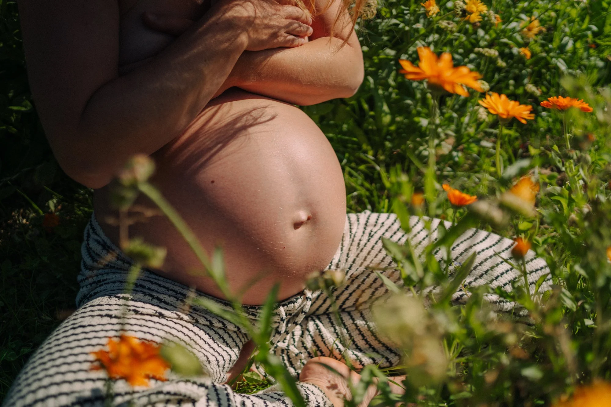 Nahaufnahme eines Babys, das in einem Feld mit orangefarbenen Blumen liegt und von einem Erwachsenen gehalten wird.