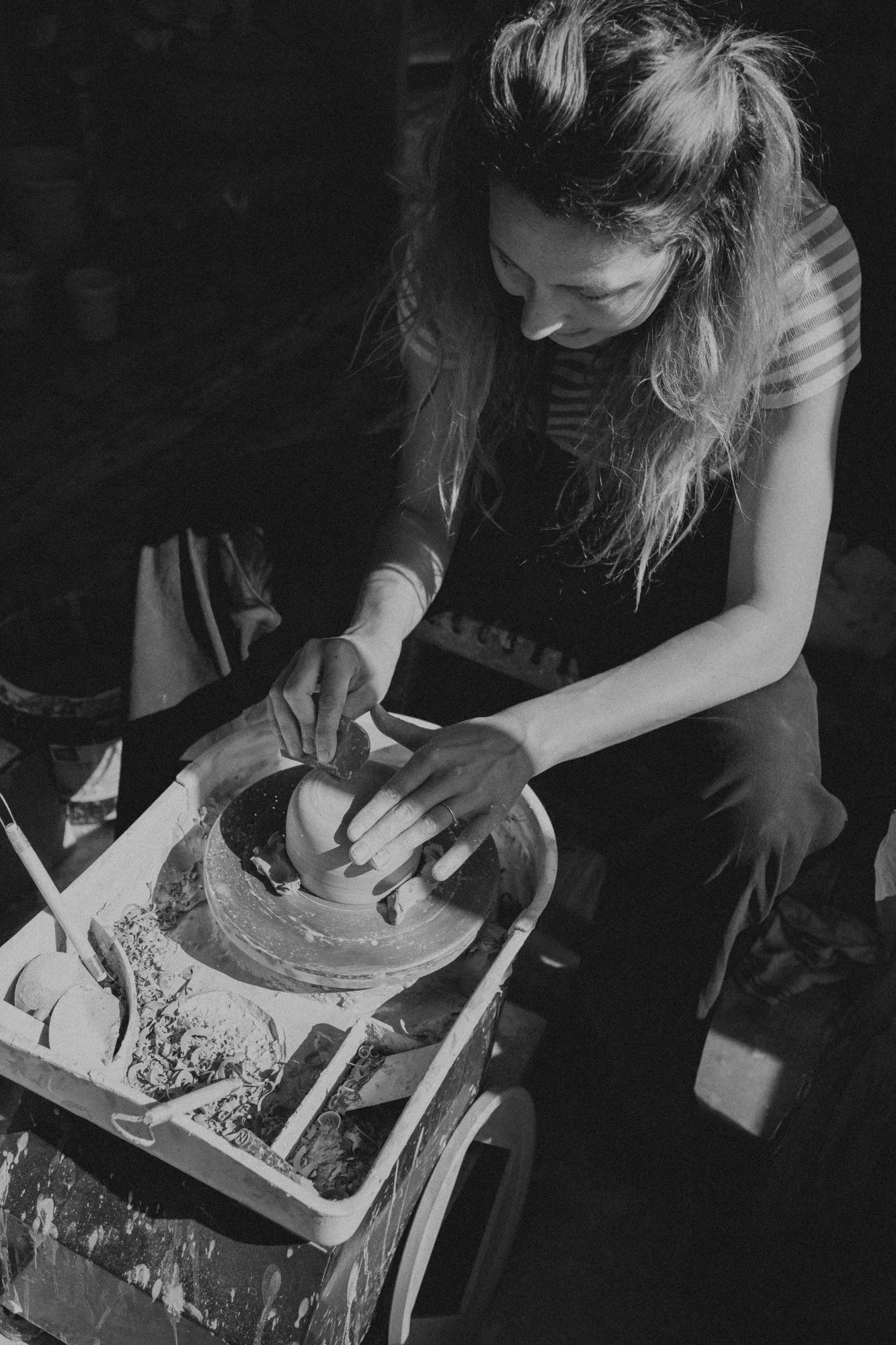 Eine Frau arbeitet artistisch an einer Töpferscheibe und formt einen Tonkrug, umgeben von Töpferwerkzeugen und Tonballen.