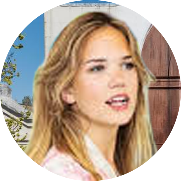 Close-up of a young woman with long, wavy blonde hair and light skin, standing outdoors near a wooden fence with trees and a building in the background.