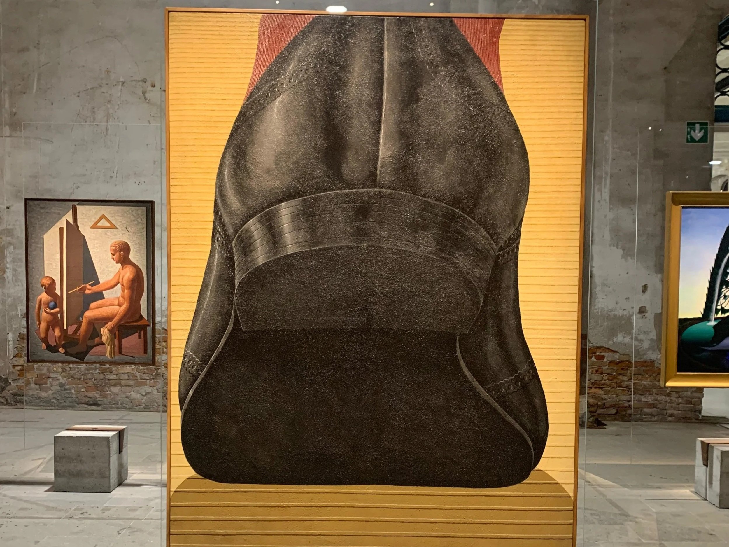 A large black and white painting of a muscular male torso, focusing on the back, displayed on a yellowish wooden panel in an art gallery.