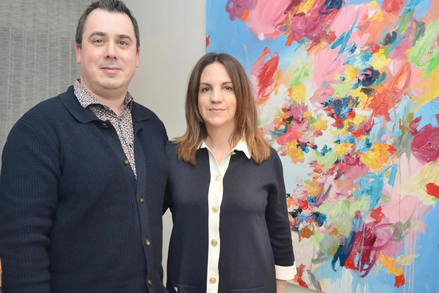 A man and woman standing side by side in front of a colorful abstract painting.