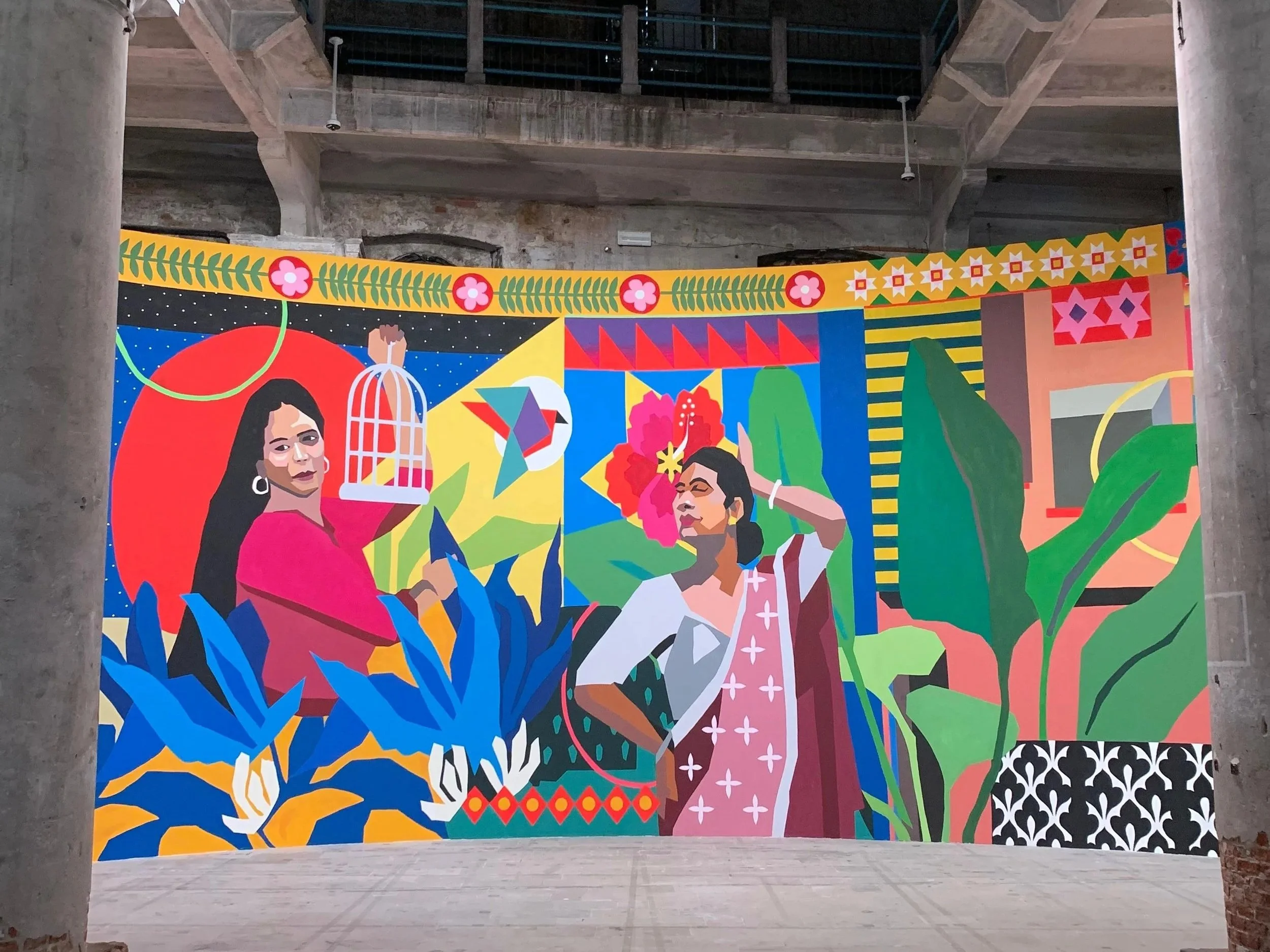 A colorful mural depicting two women surrounded by plants, flowers, and geometric patterns with a vibrant, lively style.