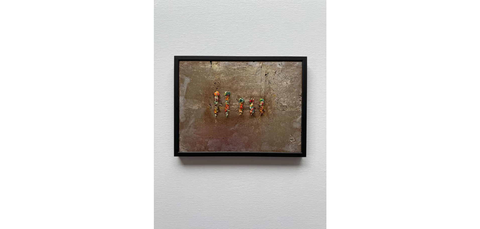 Art installation featuring colorful gummy candies arranged in vertical lines on a textured, rust-colored background, framed in black and displayed on a white wall.