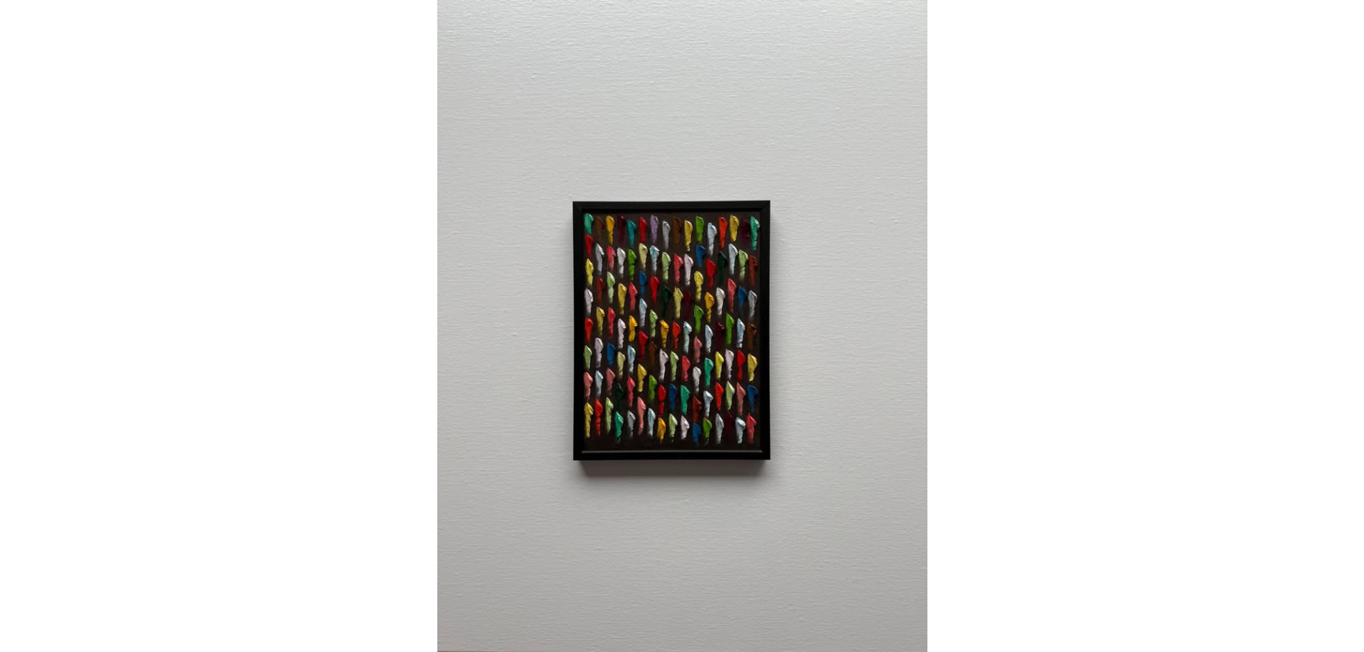 Colorful artwork featuring numerous human figures in various colors, arranged in a grid and framed in black, mounted on a light gray wall.