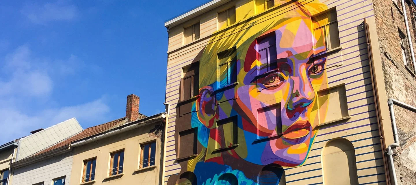 Colorful mural of a woman's face on the side of a building with a blue sky background.