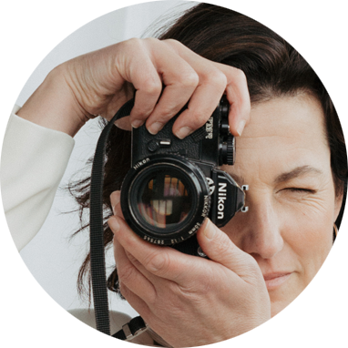 A woman taking a photo with a Nikon camera, holding it up to her face with one eye closed.