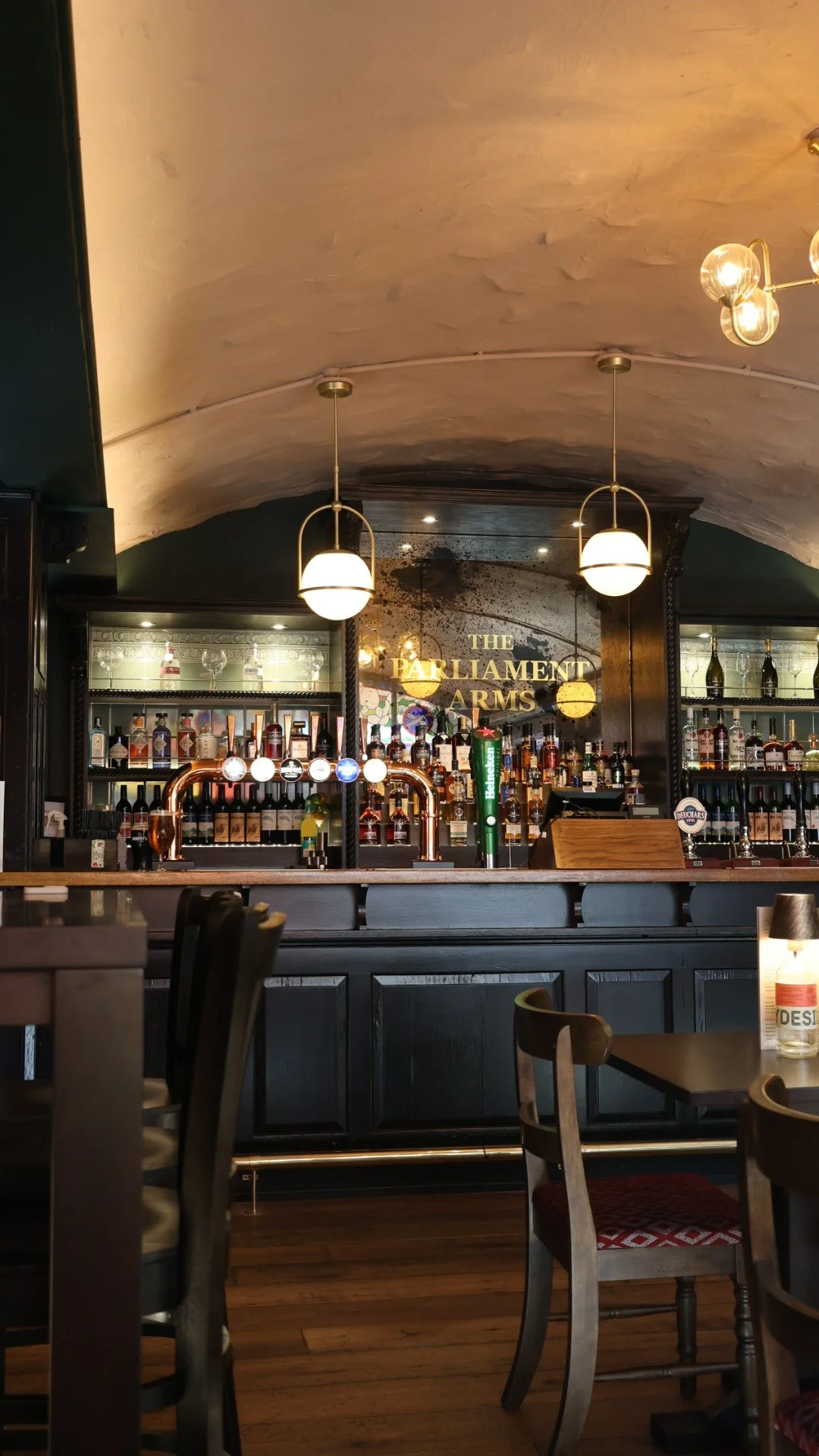 Various plates of appetizers and drinks on a wooden table, including fried croquettes, smoked salmon with lemon, slices of meat with oranges, and a dessert with berries, along with glasses of beer and cocktails.
