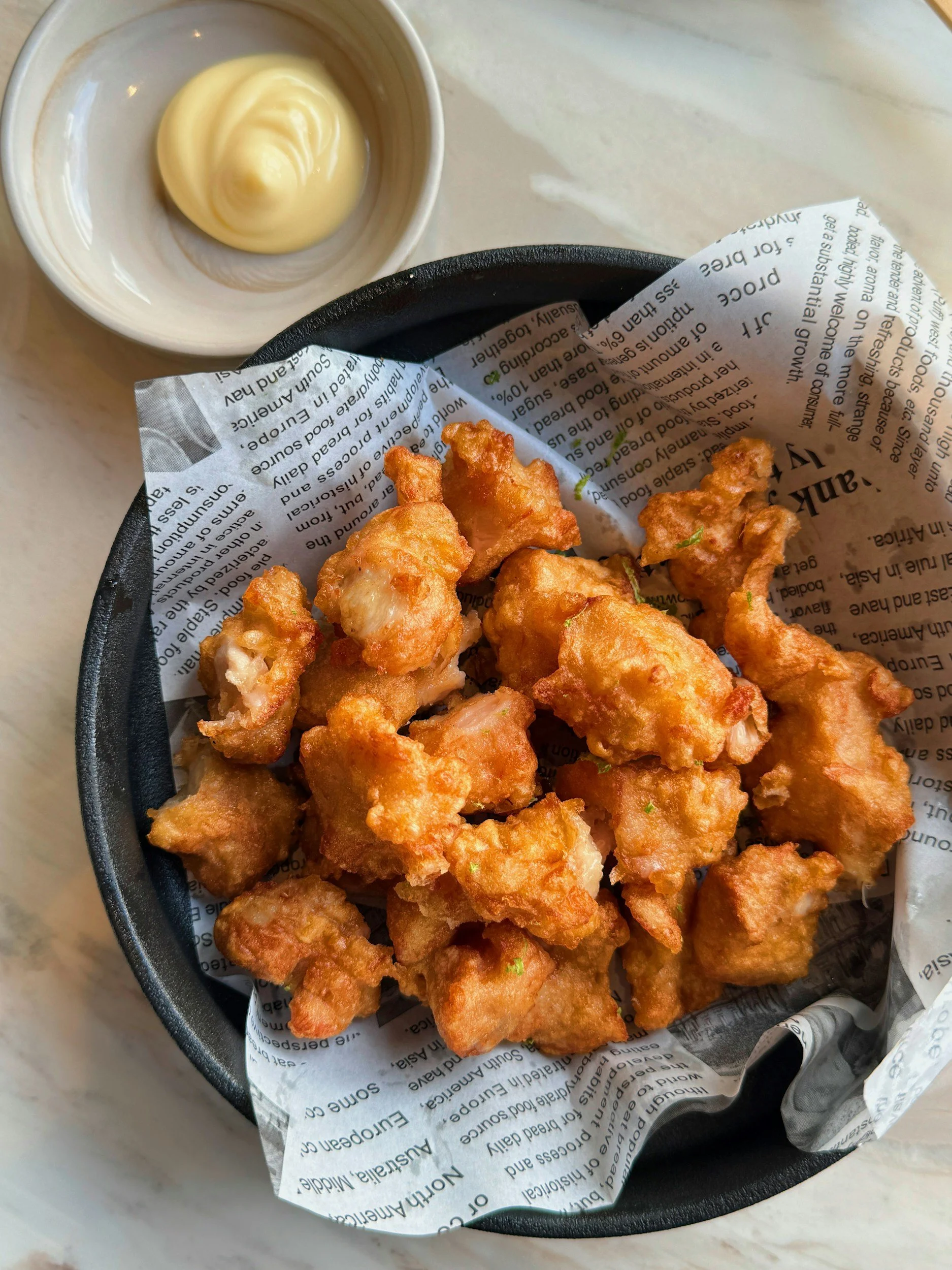 Basket of crispy fried chicken bites with a side of mayonnaise.