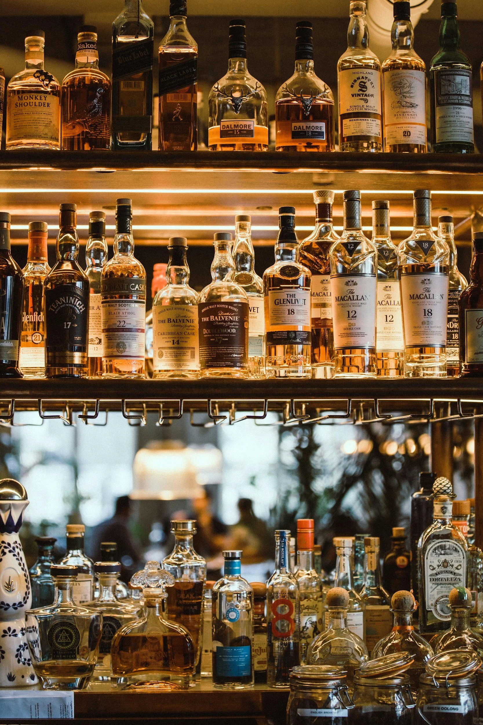 A display of various bottles of whiskey and spirits on shelves in a bar, including brands like Dalmore, Glenlivet, Macallan, and Balvenie.