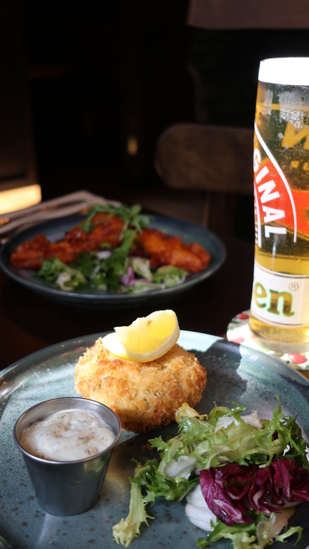 Creamy sauce being poured over two types of mashed potatoes on a white plate, with a salad in the background and drinks on the table.