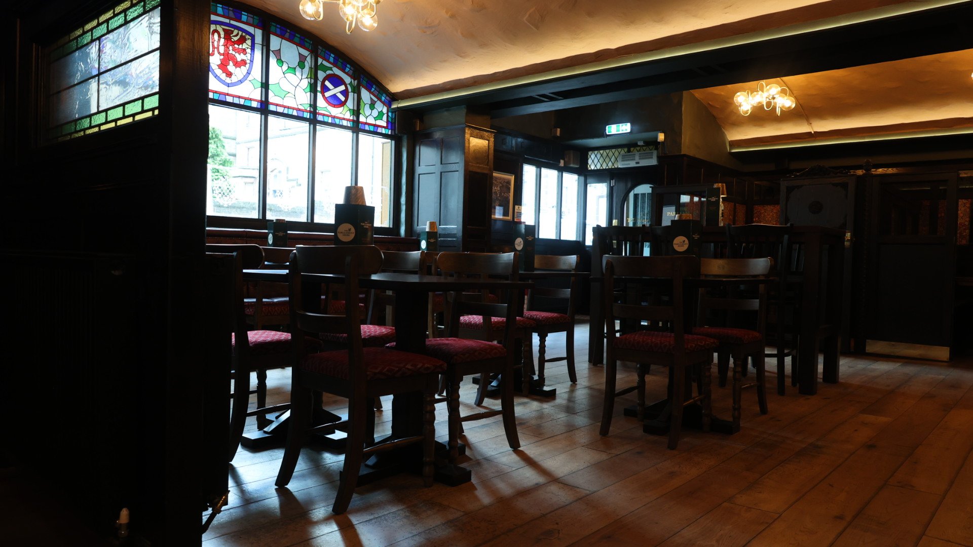 A plate with a cooked steak topped with shrimp and green herbs, side salad with cherry tomatoes and greens, and a portion of fried potatoes. In the background, a glass of red wine and a glass of white wine are visible on a wooden table.