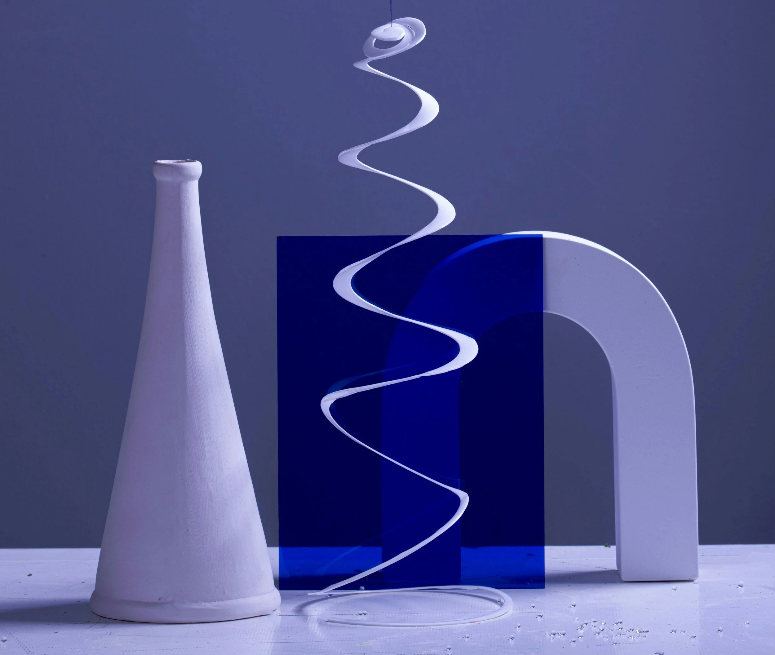 Abstract art arrangement with a white cone, a blue rectangular block, a white curved arch, and a white spiral ribbon-like shape against a gradient blue background.