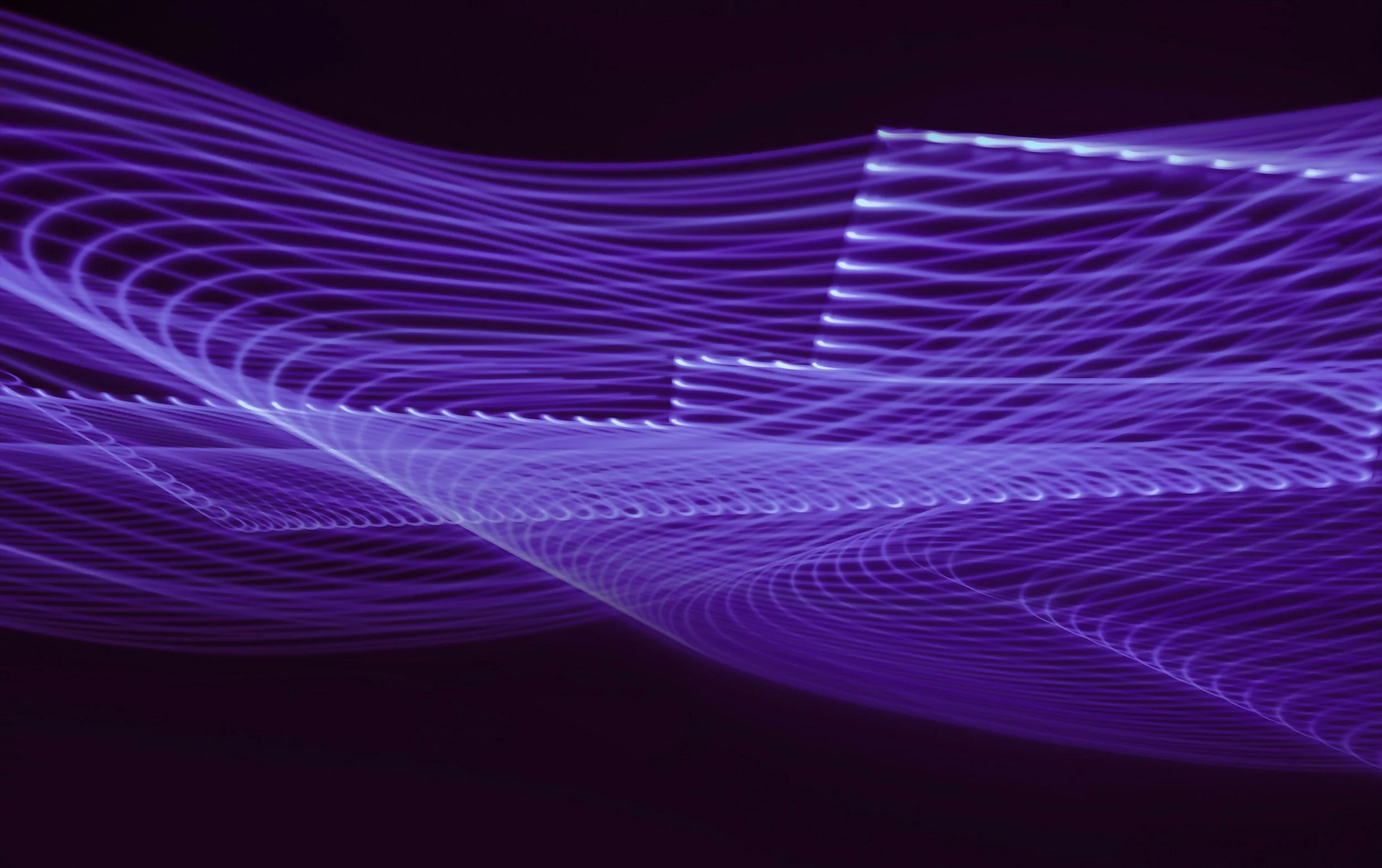 Abstract image of purple and blue light trails creating flowing patterns on black background.
