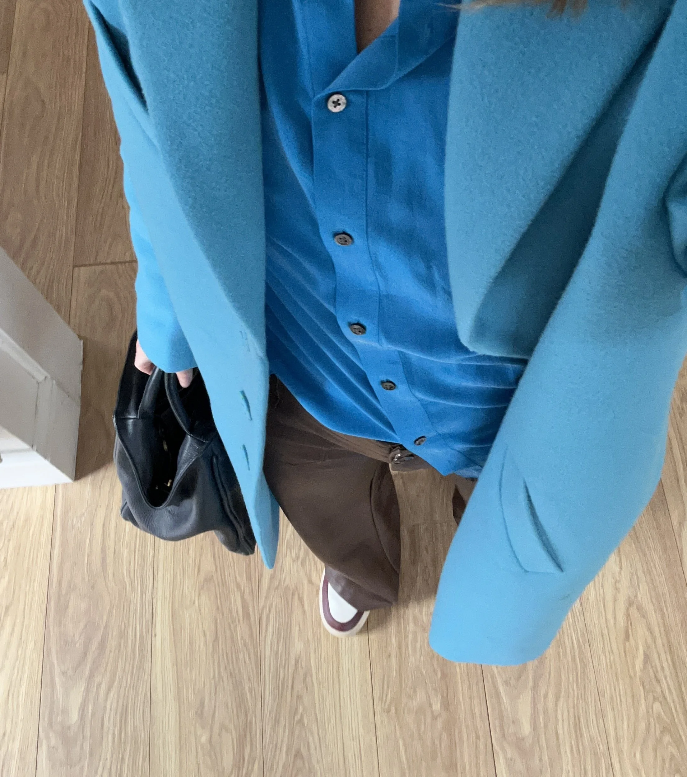 Two people shaking hands, one wearing a striped shirt and black pants, the other wearing a white shirt and beige pants, against a plain background.