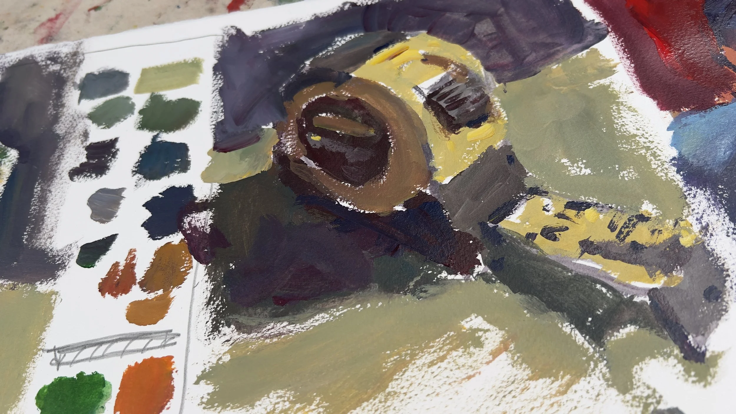 Close-up of an abstract acrylic painting with dark brown, yellow, and black brushstrokes, along with a color palette on paper showing various shades of green, blue, orange, and gray.