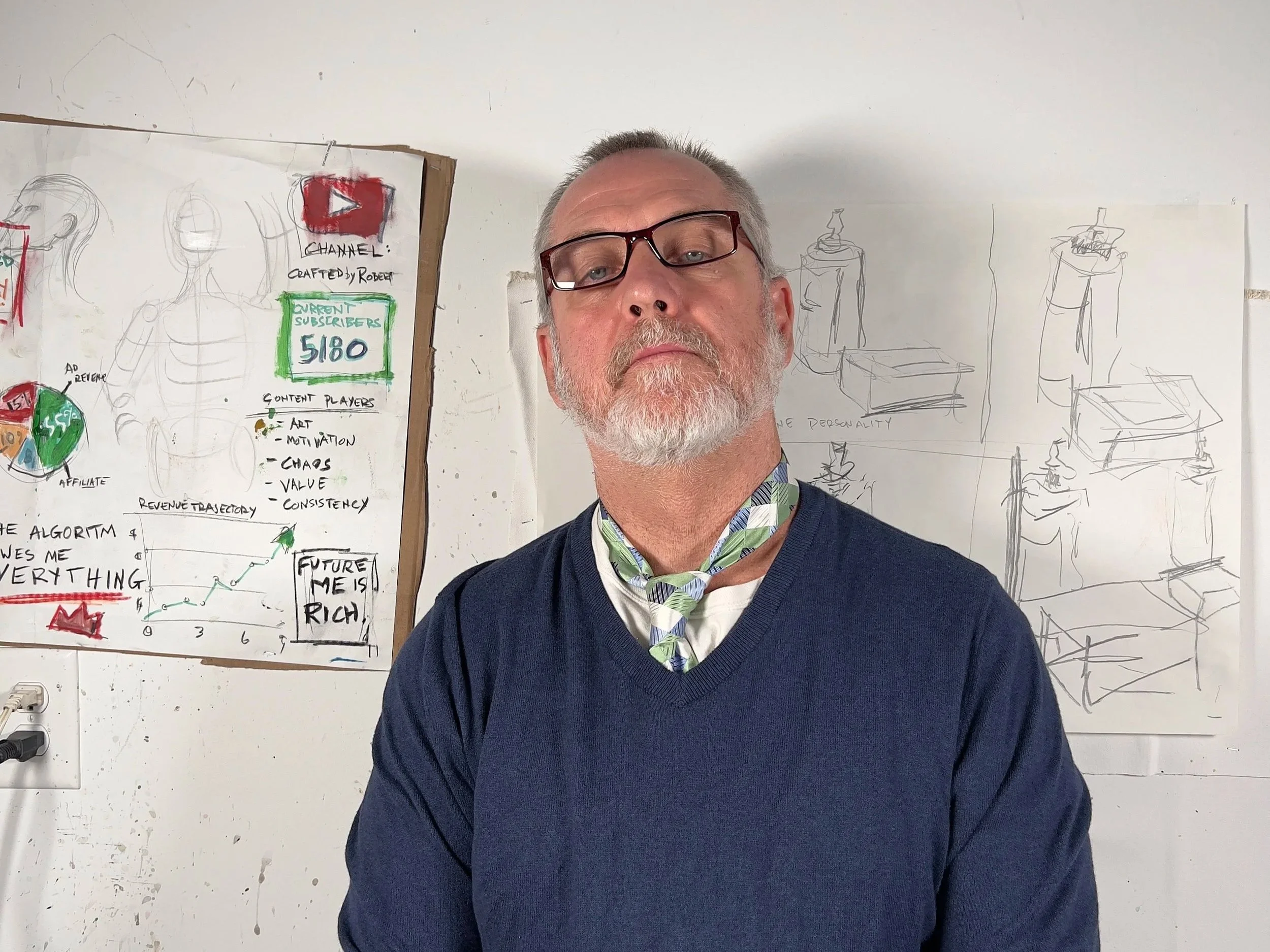 A man with glasses and a shirt with a patterned collar, standing in front of a whiteboard with sketches and notes related to content creation and audience. The room appears to be a classroom or creative workspace.