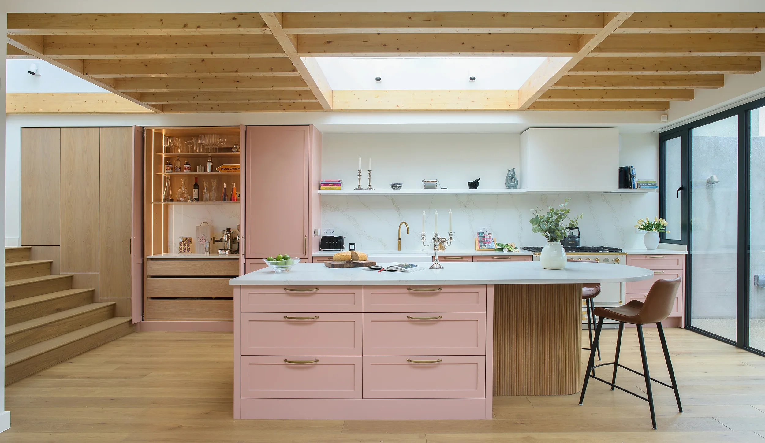 Modern kitchen with pink cabinetry, a marble island, wooden accents, and a skylight ceiling.