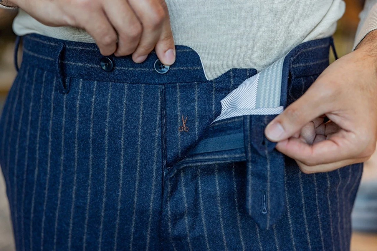 Person unbuttoning and pulling open the waistband of blue, pinstriped trousers.