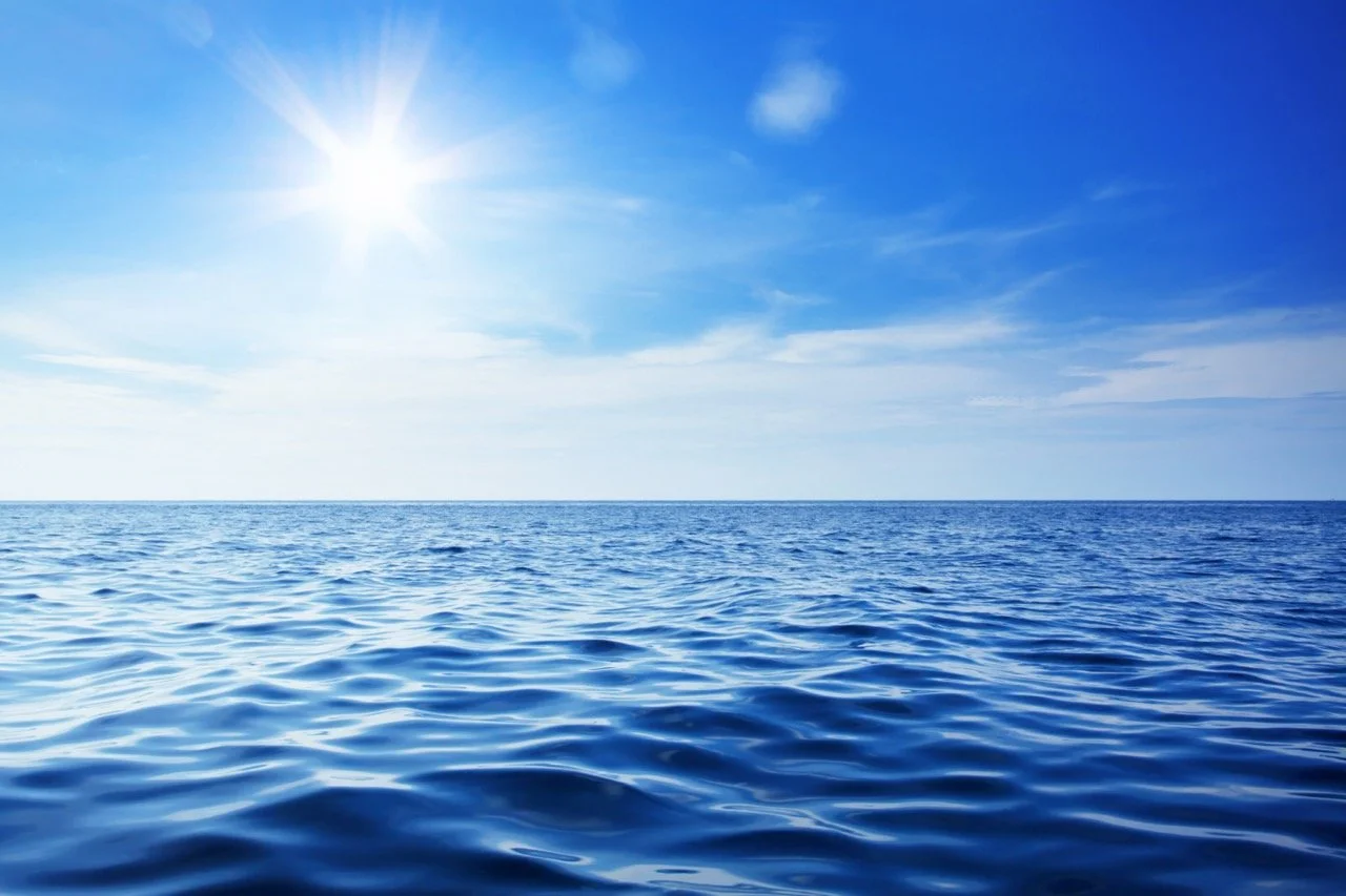 Open ocean with blue water, a clear sky, and the sun shining brightly.