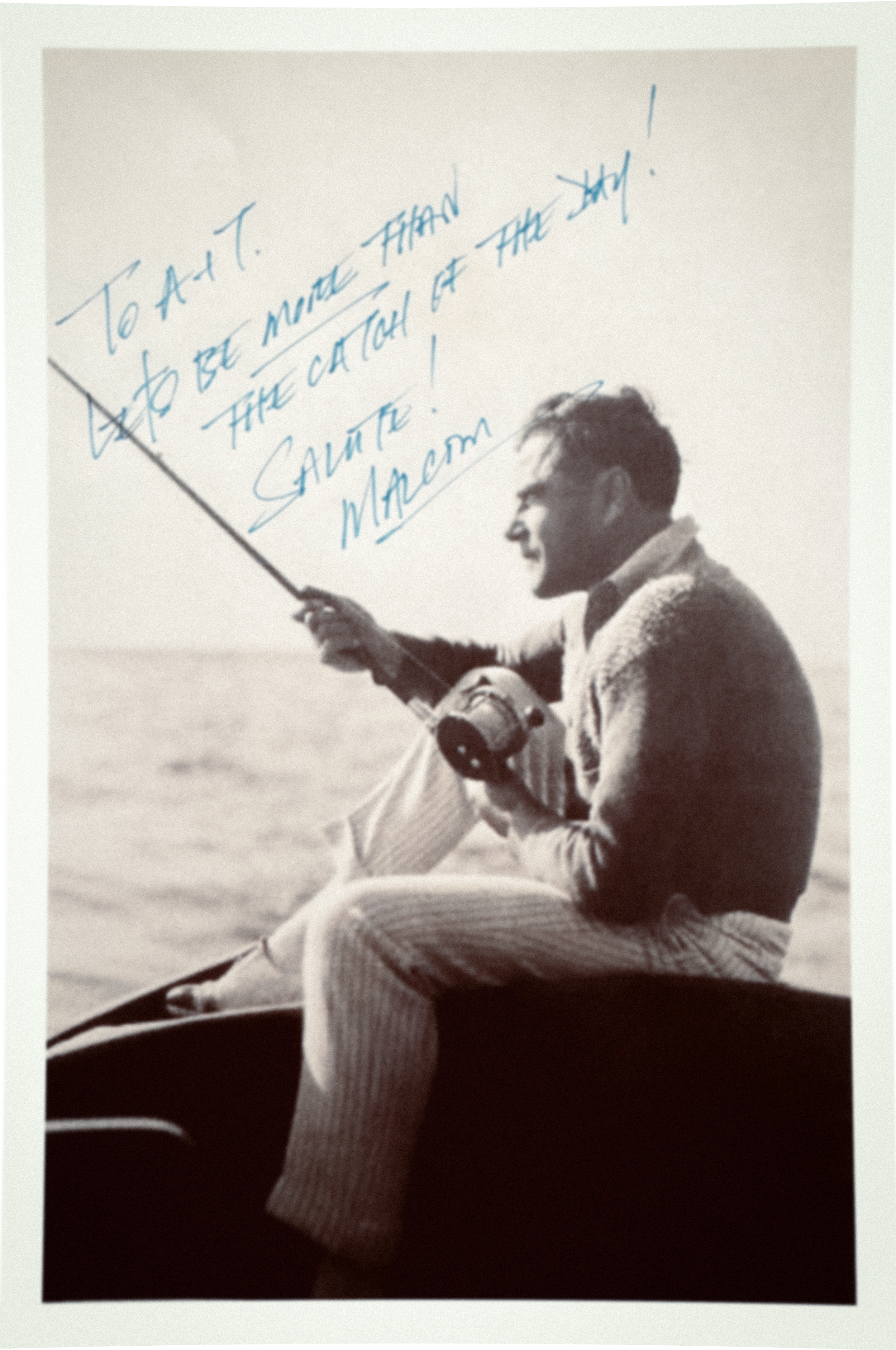 A sepia-colored photo of a well-dressed Malcom sitting on the back of a boat fishing. The photo has a handwritten note saying "To A + T, Let's be more than the catch of the day! Salute! Malcom"