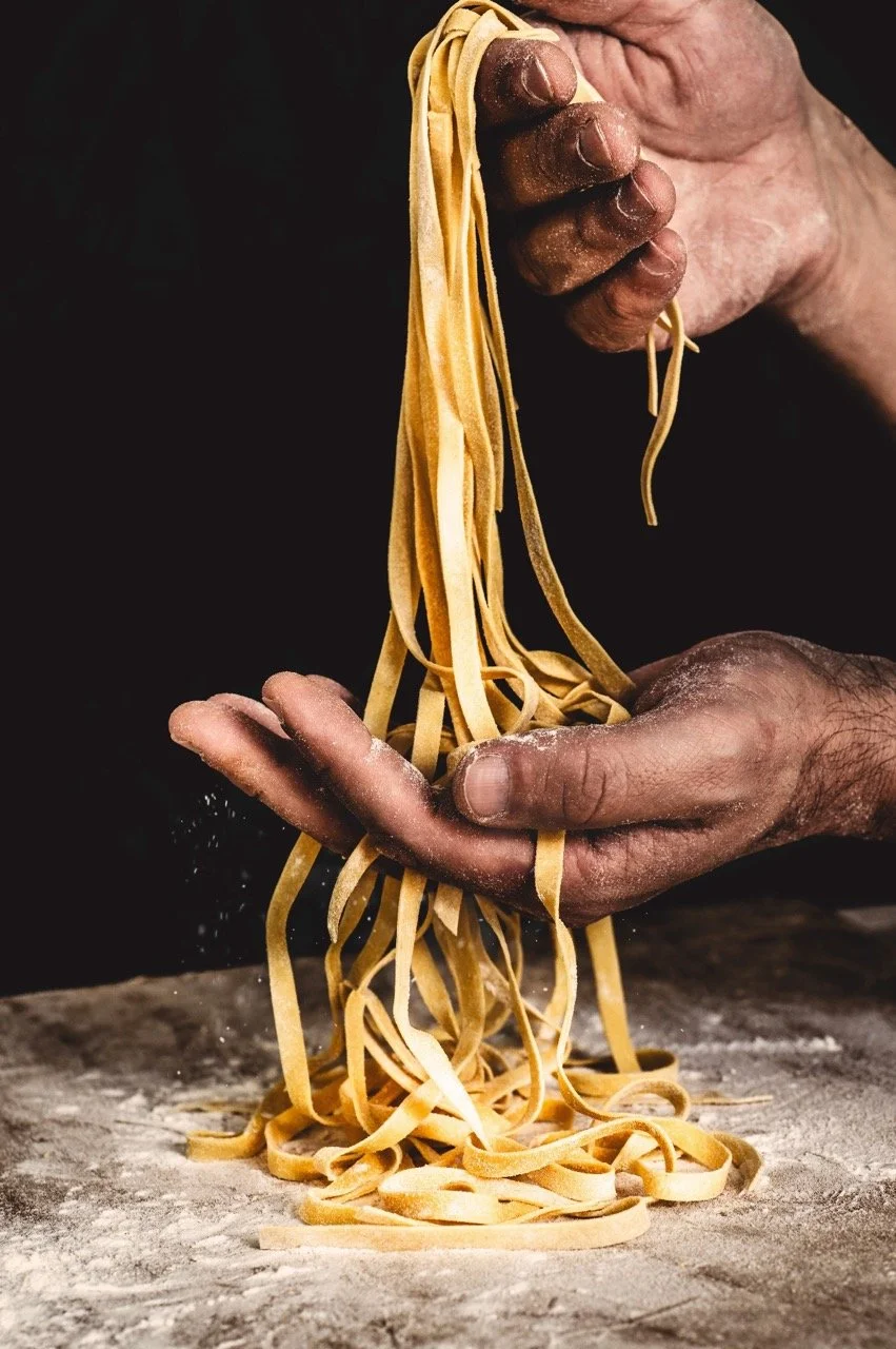 Hands holding freshly made pasta noodles over a floured surface.