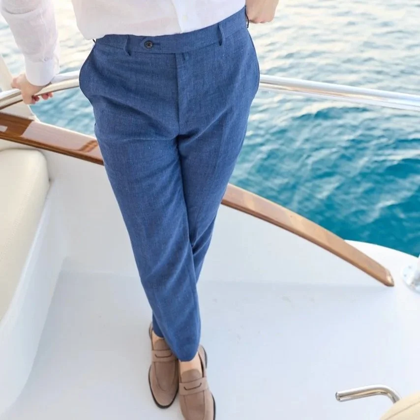 Person wearing blue dress pants and beige shoes, standing on a boat near water.