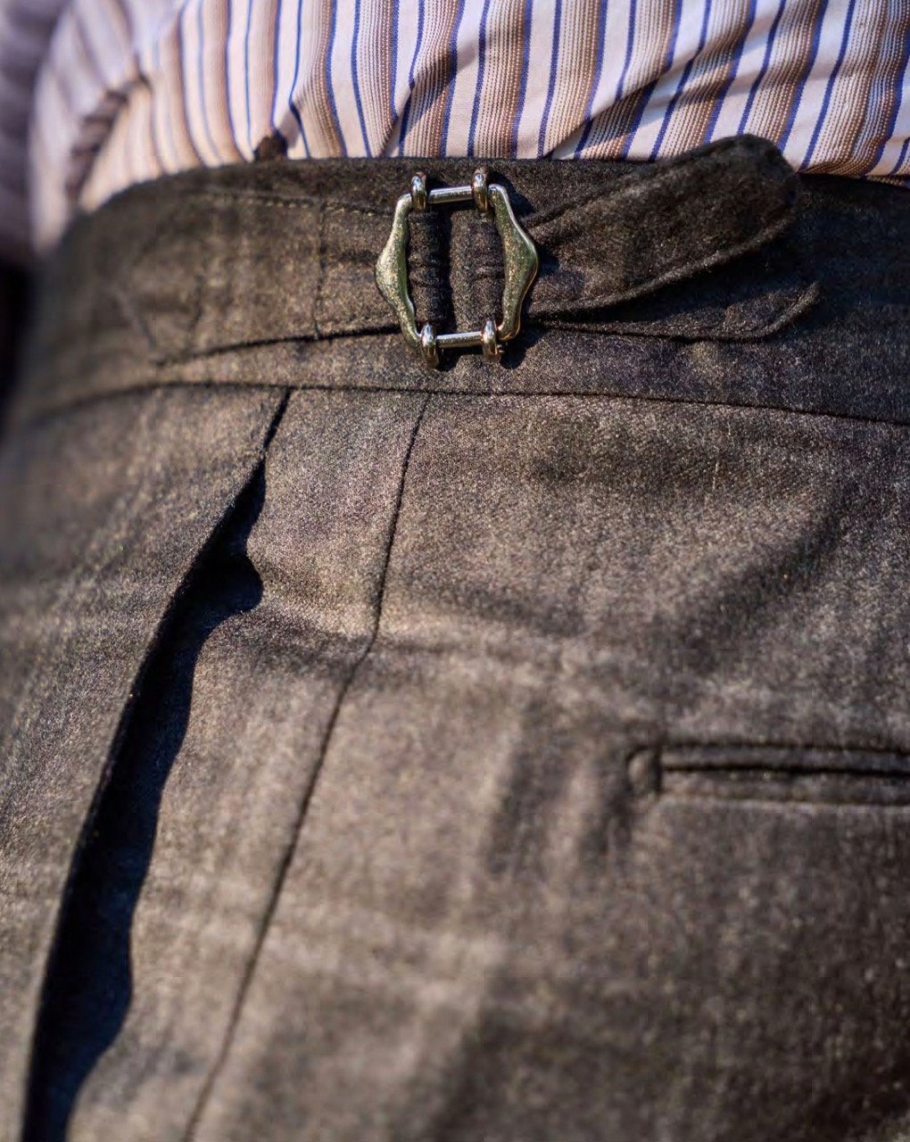 Close-up of a person's waist wearing black pants with a belt that has a silver buckle, and a striped shirt tucked in.