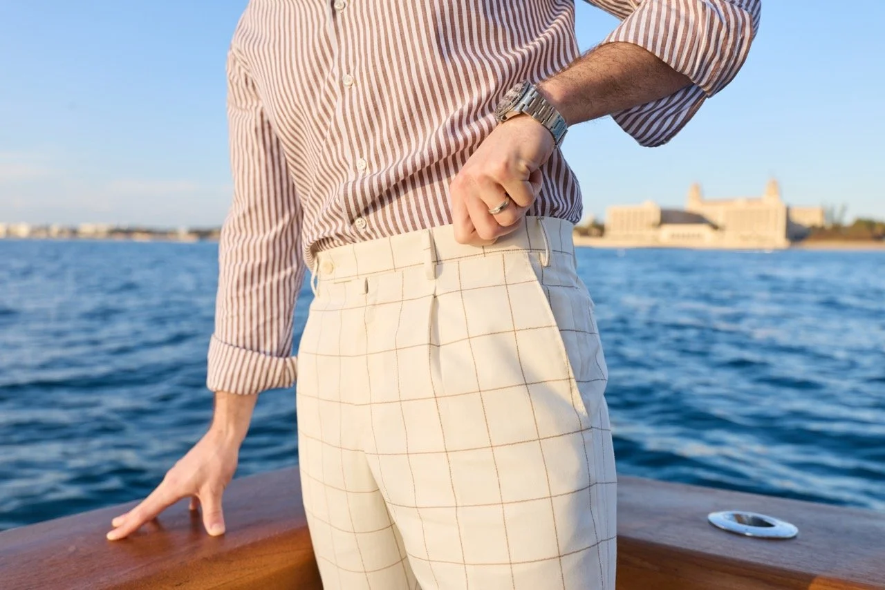 Person dressed in a striped shirt and light-colored pants standing on a boat near water, with a digital camera on the wooden surface.
