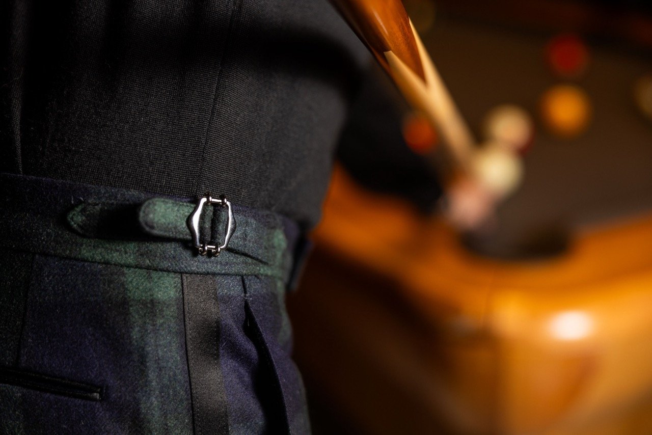 Close-up of a person's waist wearing dark plaid pants with a silver buckle belt, with a background of blurred warm-colored ovals, possibly lights.