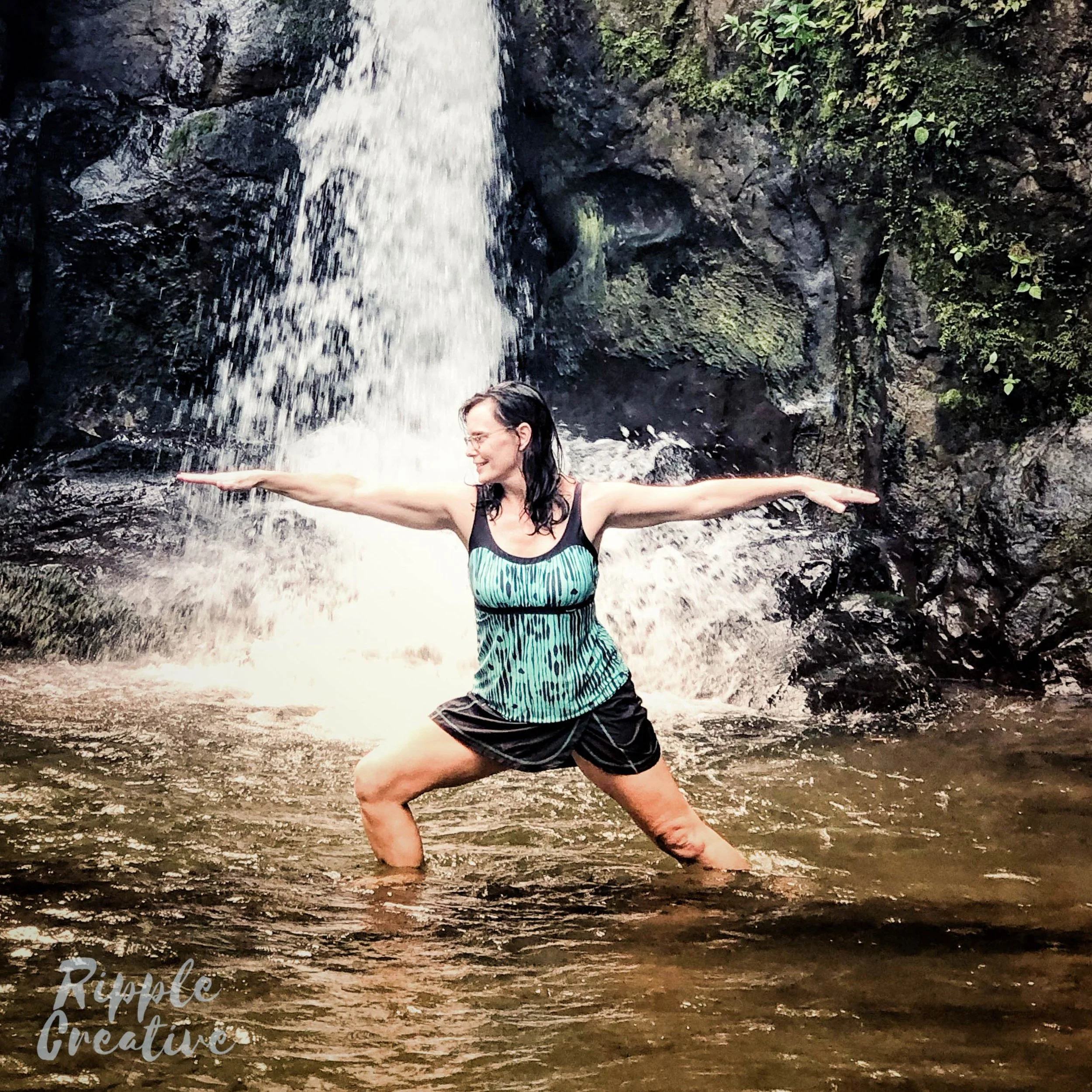 Woman practicing yoga in water at a waterfall with arms extended outward.