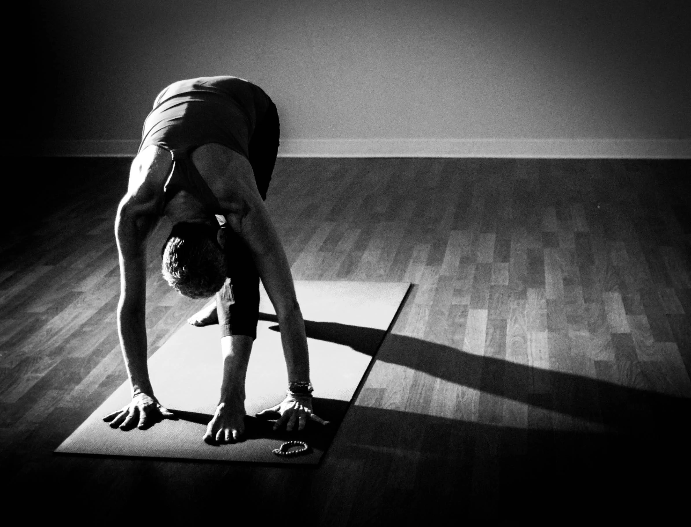 A person practicing yoga in a dimly lit room, standing on a yoga mat with their hands and feet on the ground, forming a bridge shape.
