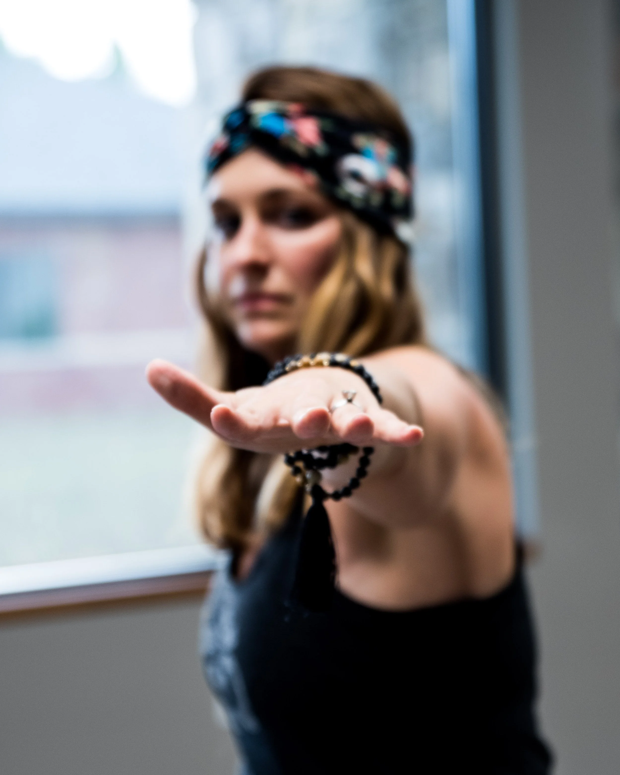 A woman wearing a floral headband and black sleeveless top extending her hand forward with a serious expression in warrior II pose.