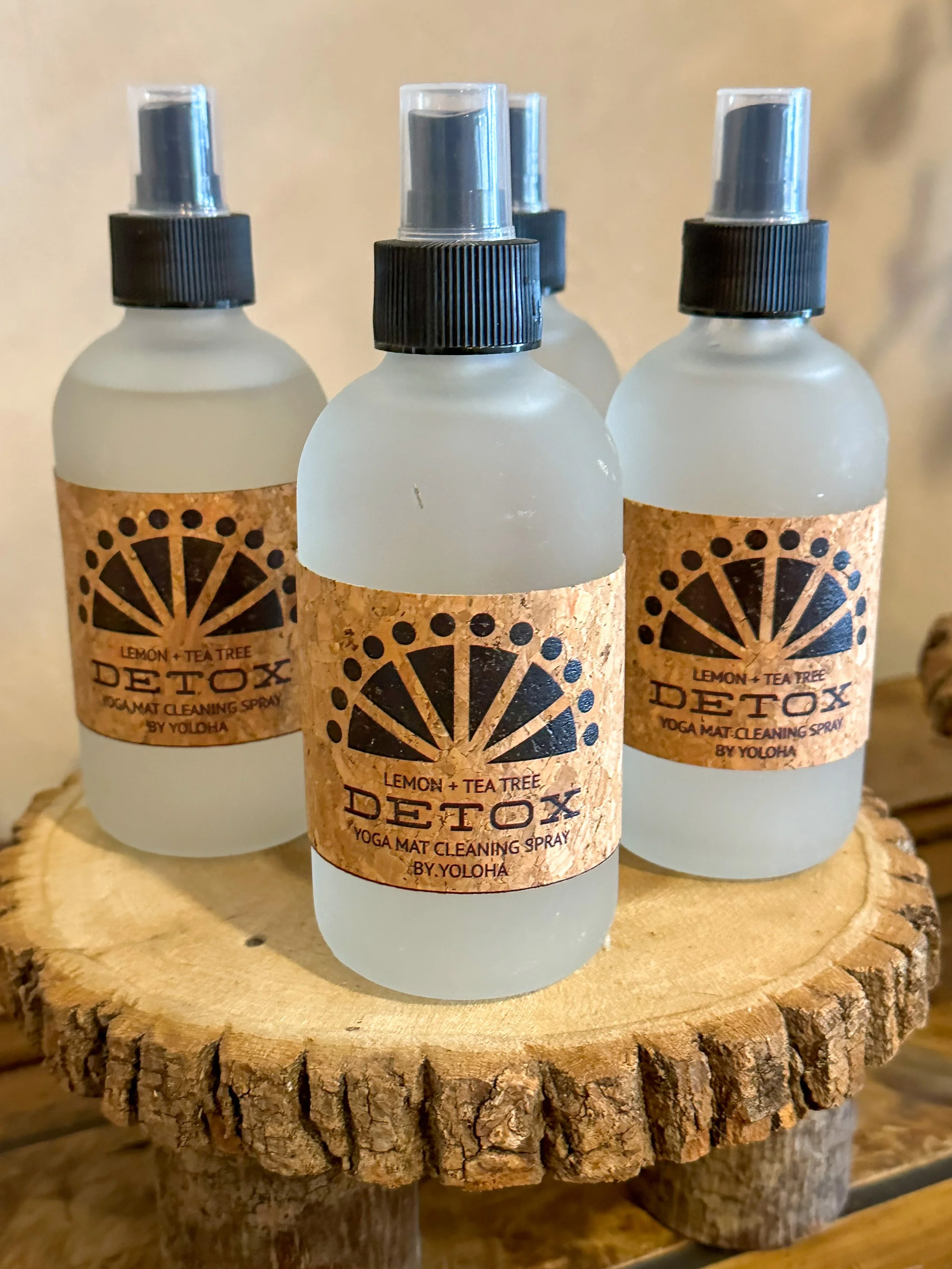 Four bottles of detox spray with lemon and tea tree labels on a wooden surface.